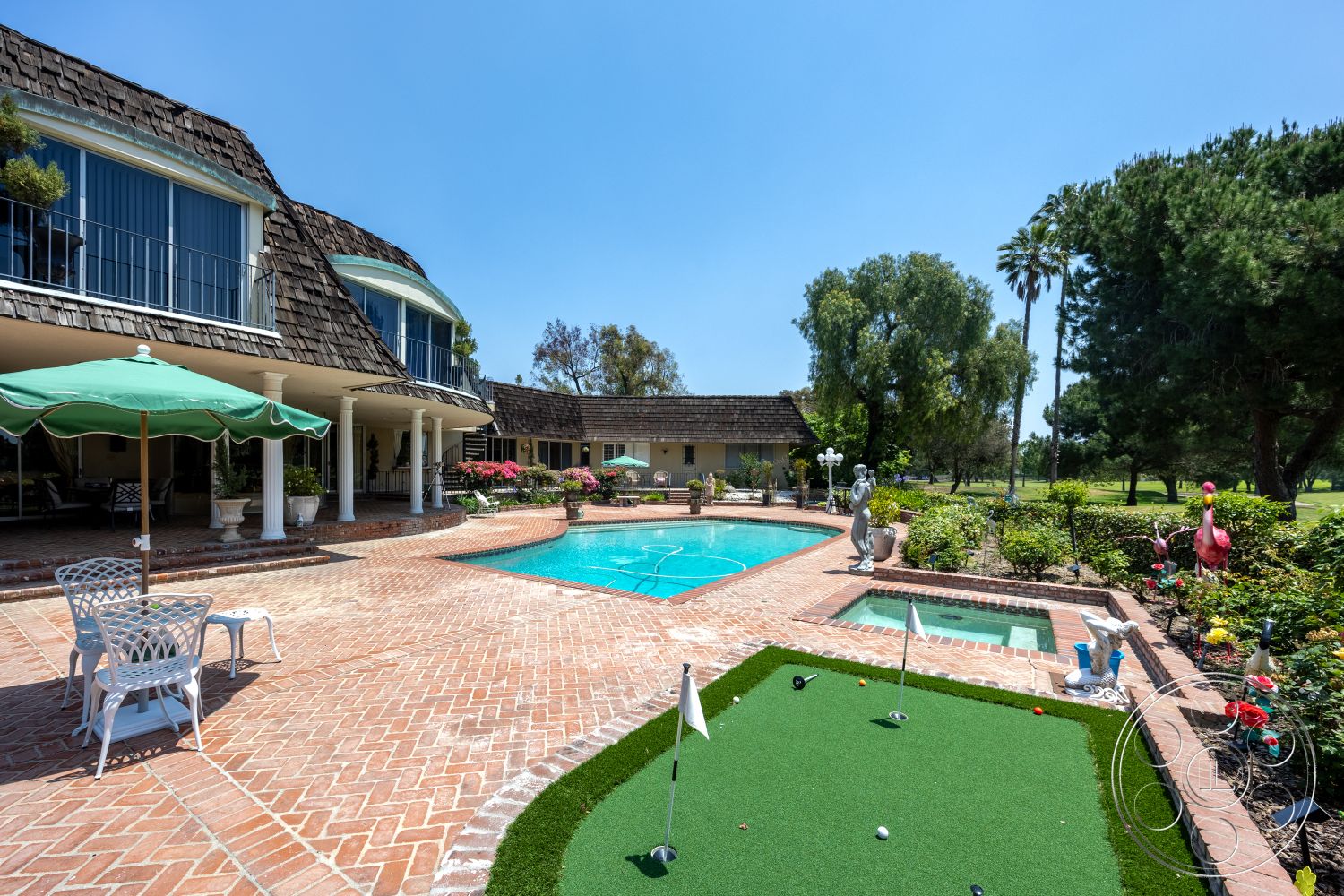Euphoria - exterior, palm trees, rectangular swimming pool, floor-to-ceiling windows, circular hot tub, flowering shrubs, tropical landscaping, shingle roof, outdoor umbrella, brick patio flooring, decorative garden statues, green artificial grass putting green, white metal outdoor furniture