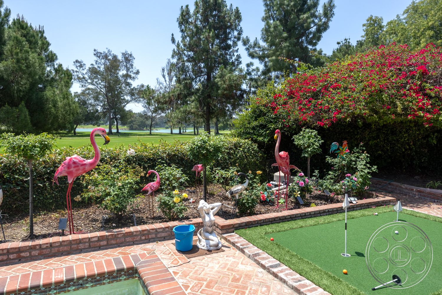 Euphoria - exterior, lush garden setting, flowering shrubbery, brick patio flooring, decorative stone borders, mature trees in background, synthetic turf putting green, pink flamingo garden ornaments, brick flower bed edging, golf putting area, open green space view