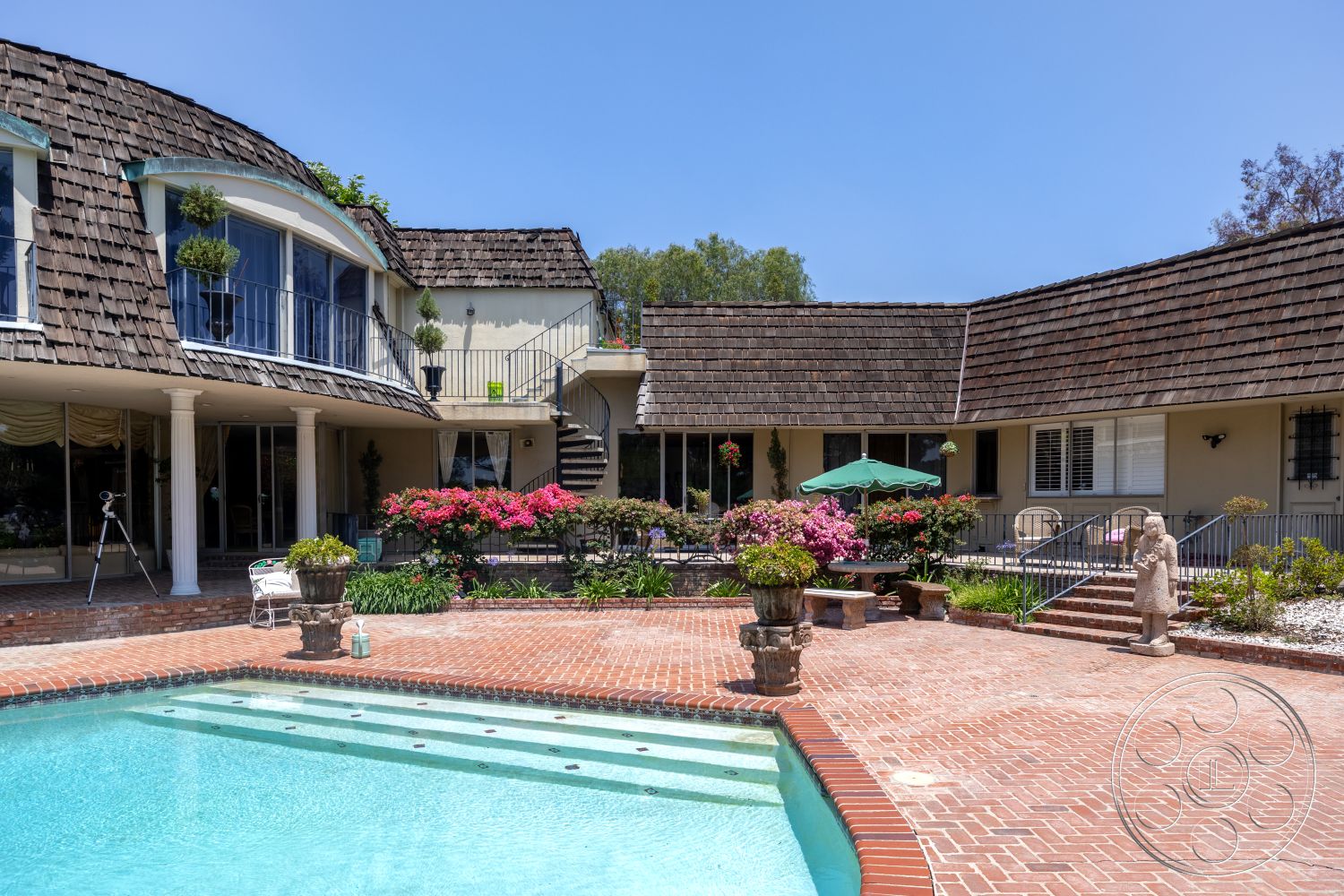 Euphoria - exterior, brick walkway, flowering plants, arched doorways, rectangular pool, shingle roof, two-story home, corner windows, landscaped garden area, concrete pool border, brick patio flooring, metal stair railing, wooden balcony railings, decorative stone statues