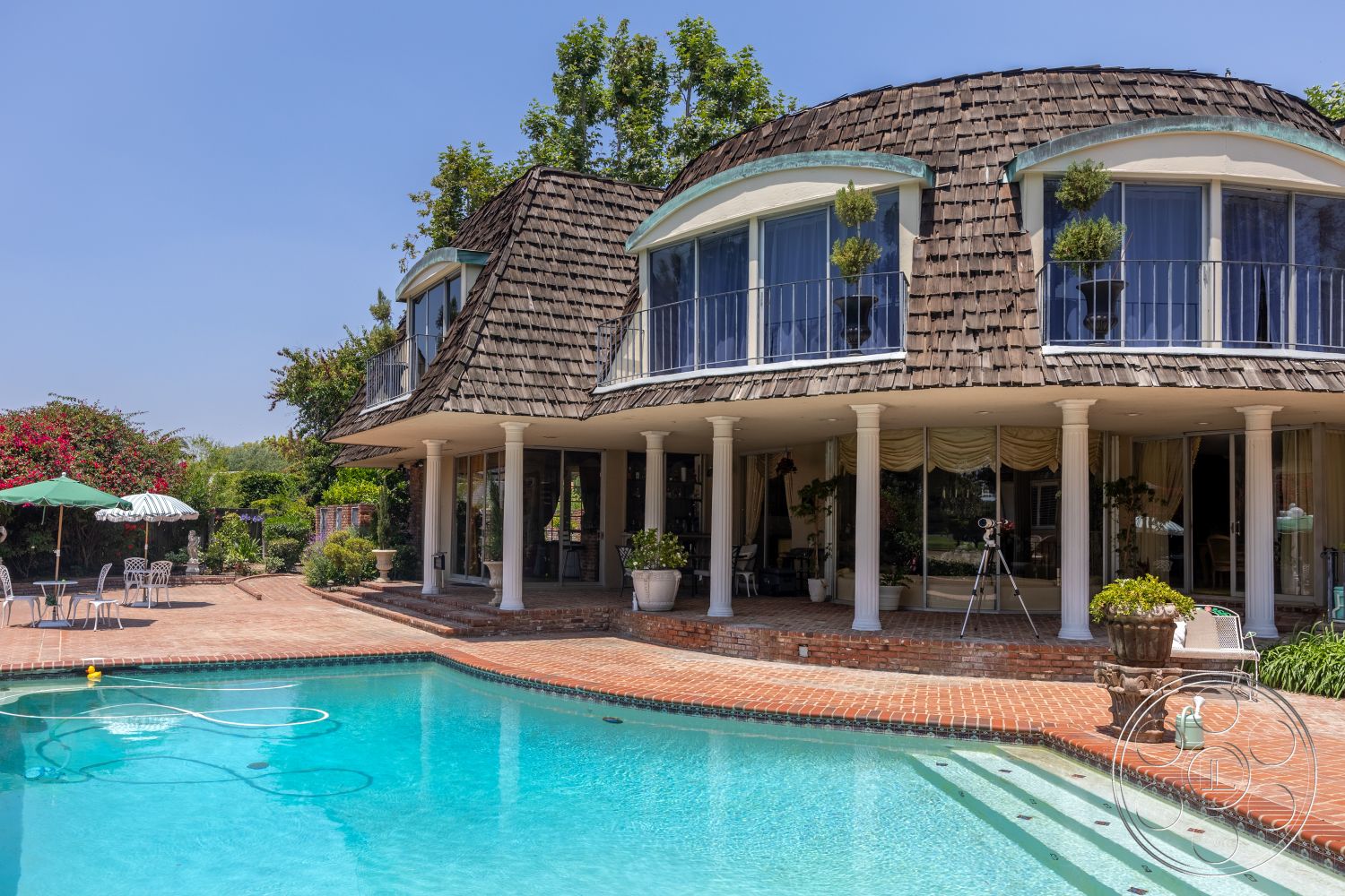 Euphoria - exterior, lush greenery, decorative planter, outdoor dining area, round windows, rectangular pool, shingle roof, outdoor umbrella, landscaped garden setting, concrete pool border, brick patio flooring, glass balcony railings, textured exterior walls, columns with white paint, sloped roof shape