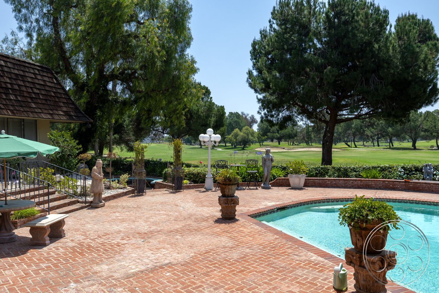 Euphoria - exterior, landscaped garden, potted plants, decorative sculptures, rectangular swimming pool, stone planters, outdoor lighting fixtures, wooden outdoor furniture, brick patio flooring, sloped shingle roof, green golf course view, metal railing stairs, large outdoor umbrella