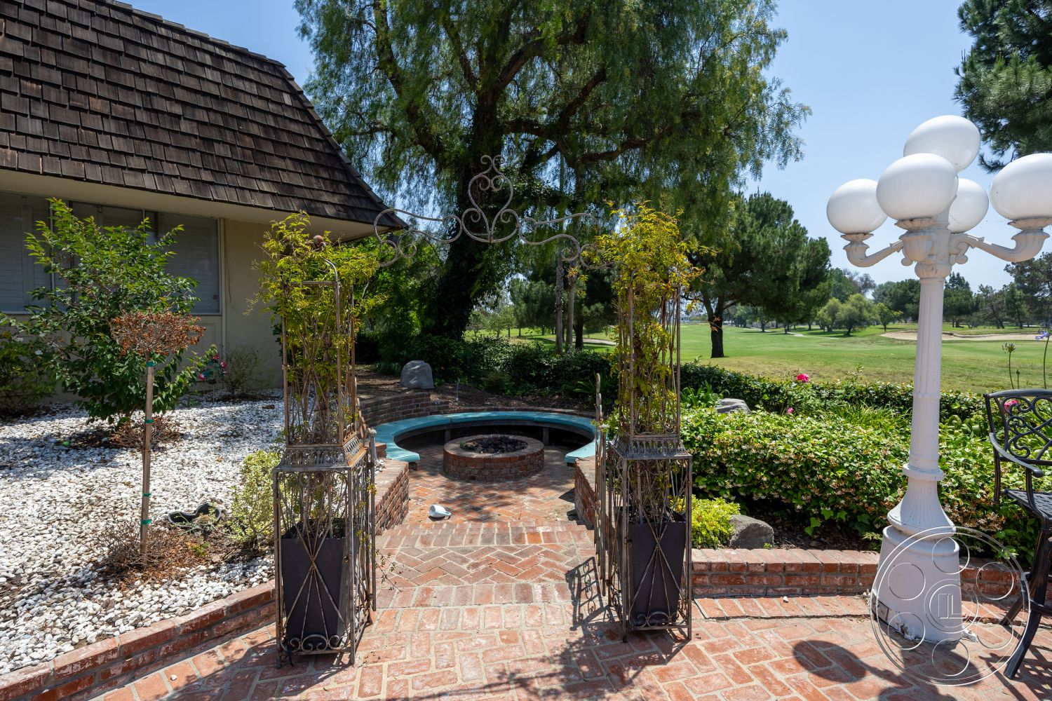Euphoria - exterior, shingle roof, planted flower beds, lush green landscaping, circular fire pit, brick patio flooring, golf course view, stone garden features, metal trellis planters, decorative street lamp, round pool with water feature