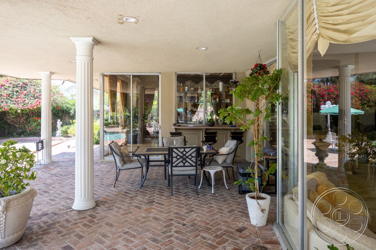 Euphoria - exterior, glass sliding doors, outdoor seating area, planter with greenery, exposed ceiling beams, decorative stone planters, brick patio flooring, surrounding garden foliage, pillared porch structure, bar area with glass shelving