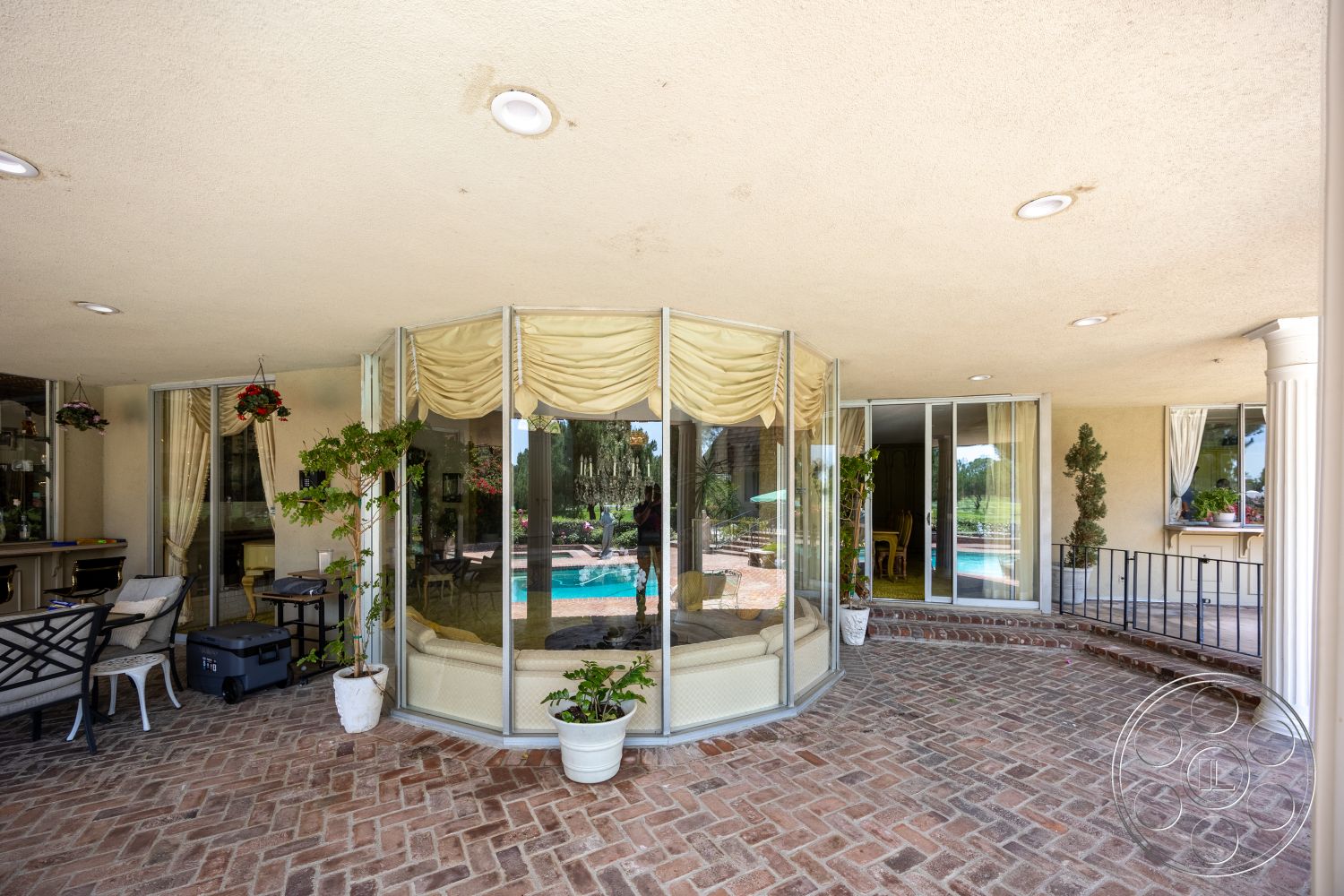 Euphoria - exterior, open floor plan, potted plants, outdoor dining area, decorative planters, light-colored stucco walls, elegant drapery, recessed ceiling lighting, lush garden setting, brick patio flooring, sunlit outdoor space, rounded seating area, columned support structure, curved glass wall enclosure, in-ground swimming pool view