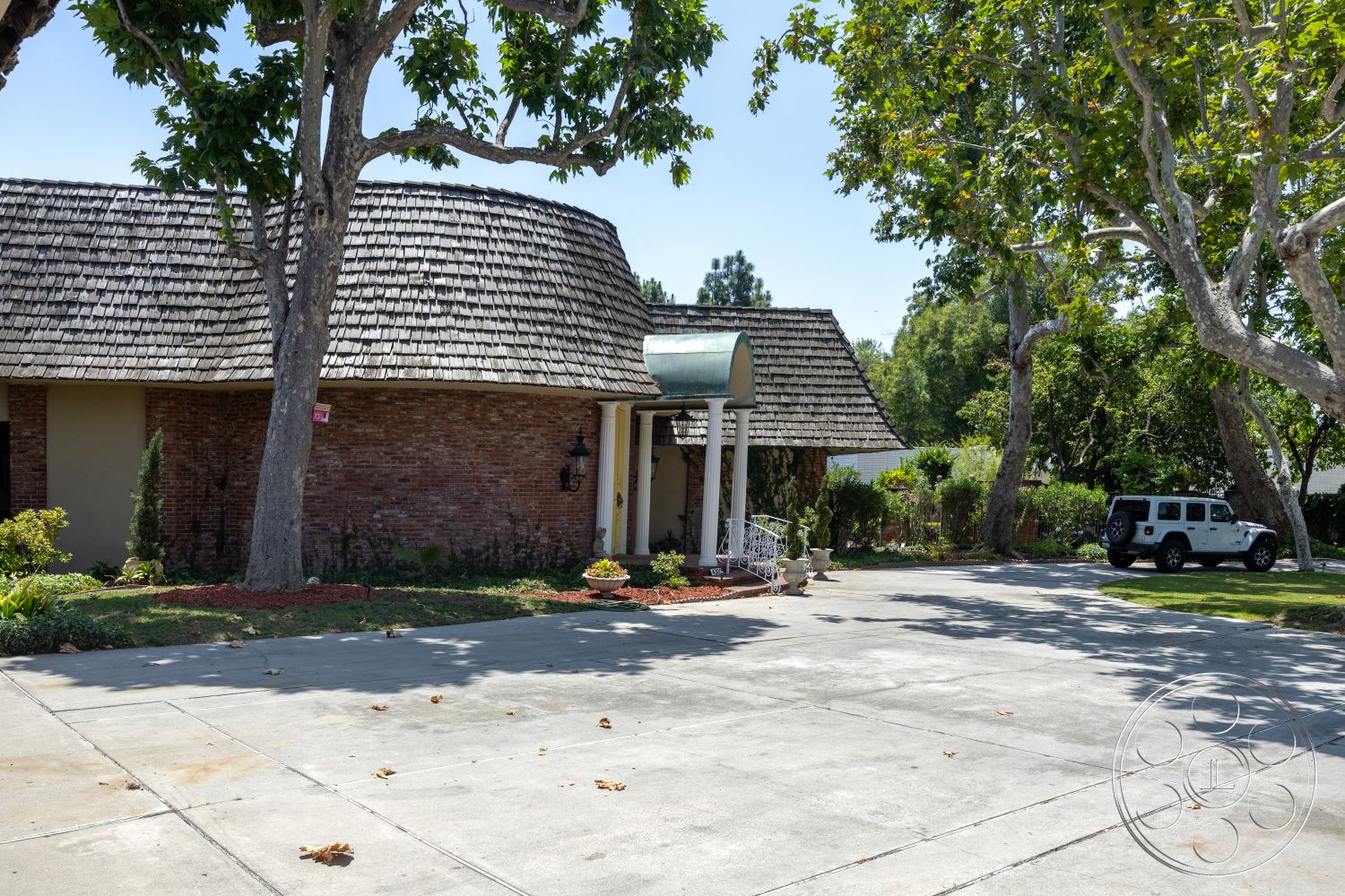 Euphoria - exterior, mature trees, brick walls, concrete driveway, decorative railing, shingled roof, landscaped garden area, brick flower bed border, wooden porch columns, curved roof shape
