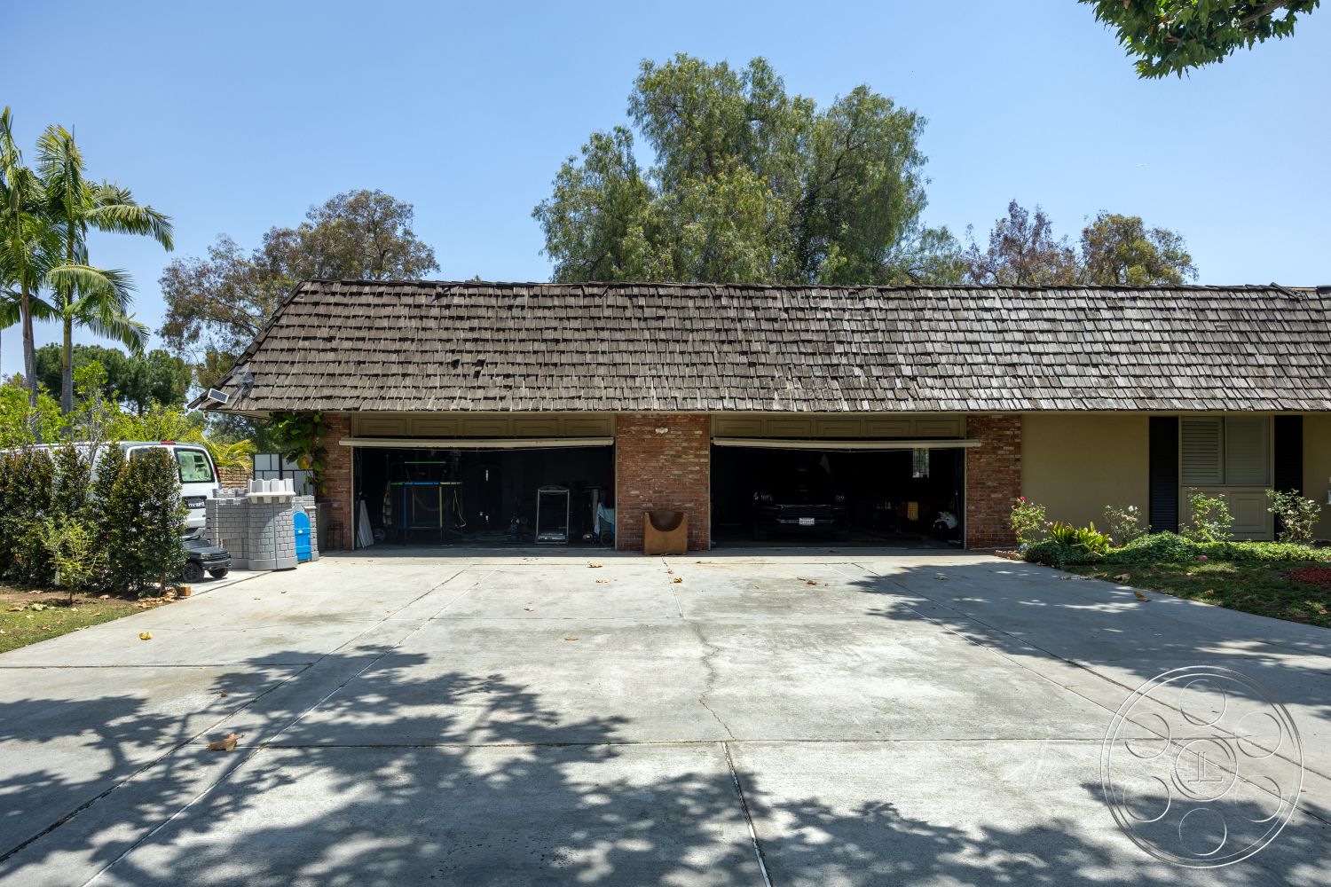 Euphoria - exterior, asphalt shingle roof, concrete driveway, minimalist landscaping, flat roof design, landscaped garden with shrubs, open garage space, brick garage wall, tile patio floor, single-story garage, overhead garage door, palm trees in the background, crushed stone decorative accents