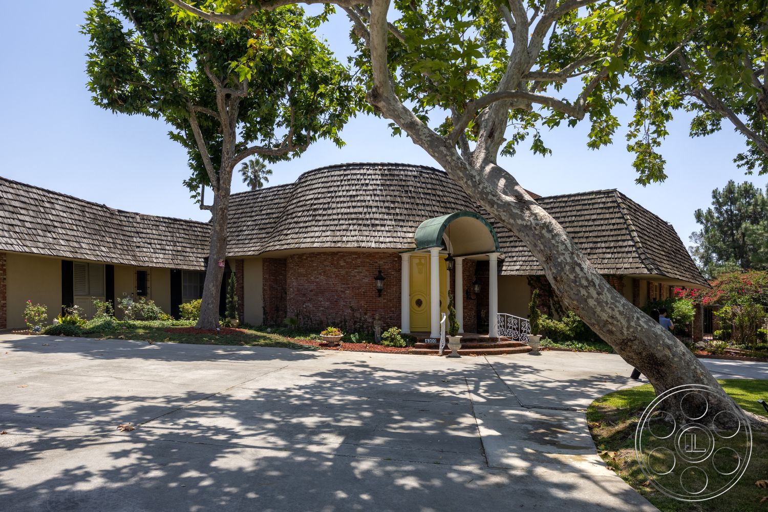 Euphoria - exterior, landscaped garden, asphalt shingle roof, brick accent wall, lush green lawn, concrete driveway, arched entryway, evergreen trees, curved roof, wooden porch columns, circular entrance patio, large canopy over entrance