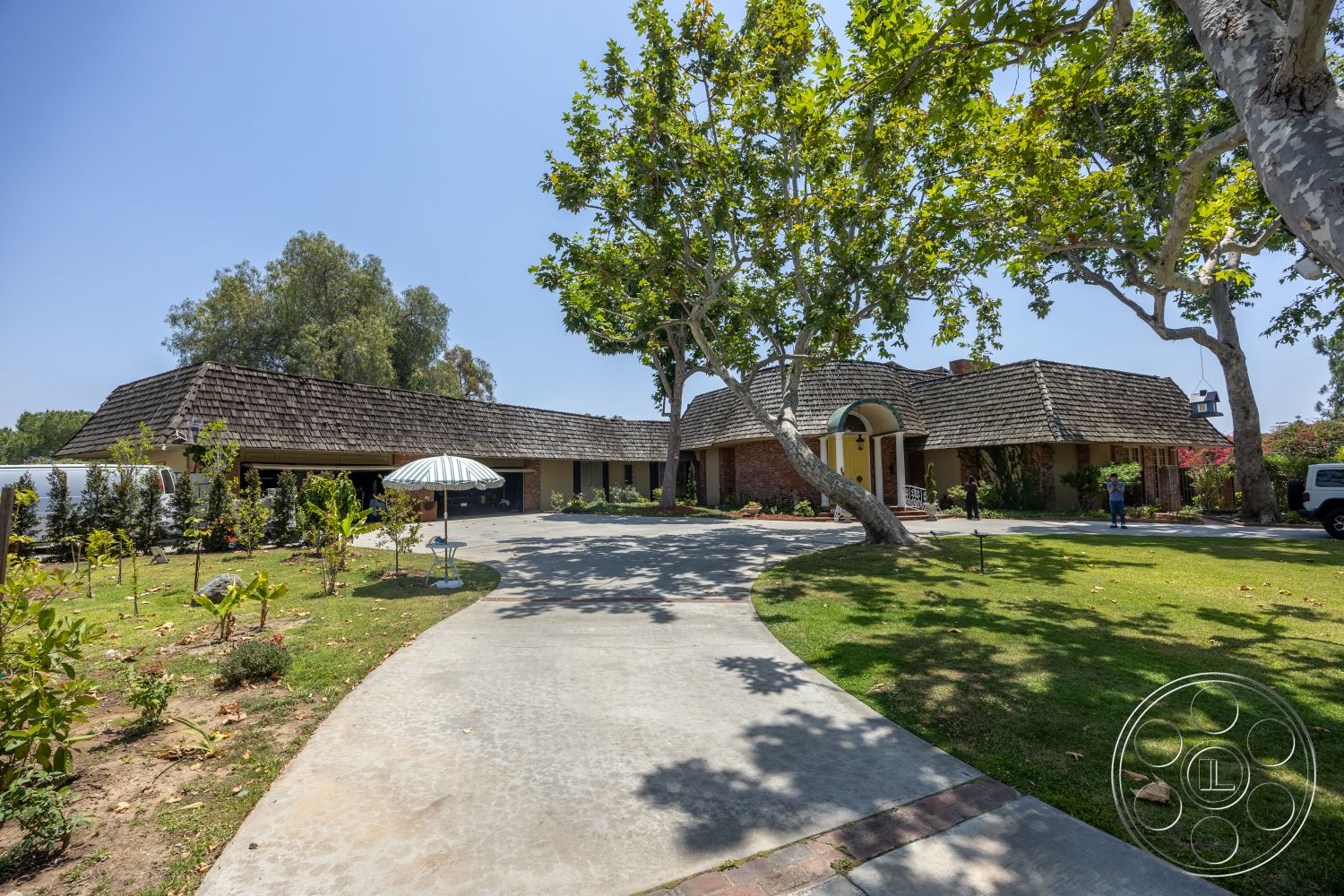Euphoria - exterior, landscaped garden, stone accent wall, urban setting, single-story home, lush green lawn, concrete driveway, curved driveway, arched entryway, outdoor patio area, brick exterior walls, mature shade trees, wood shingle roof
