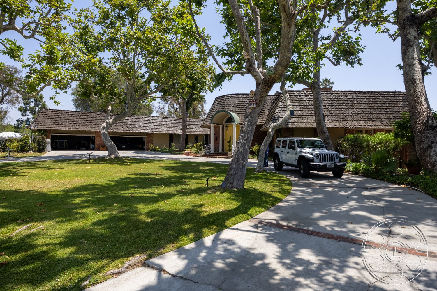 Euphoria - exterior, landscaped garden, concrete driveway, curved driveway, manicured lawn, shingle roof, ranch-style home, front porch area, mature shade trees, brick garage façade, arched front entrance