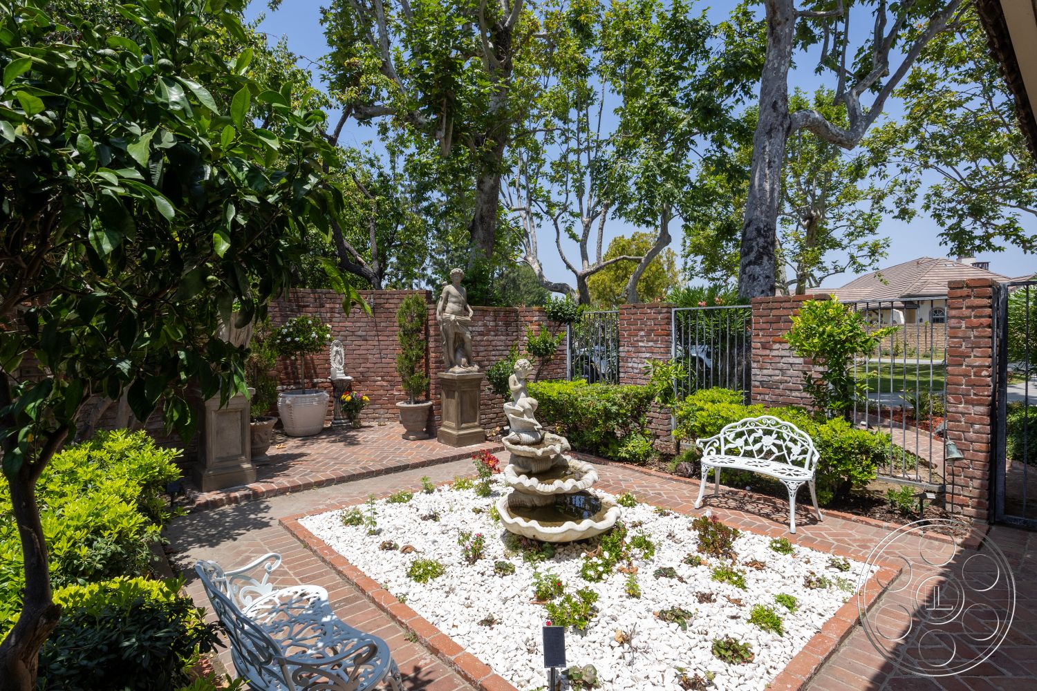 Euphoria - exterior, flowering plants, decorative stone planters, ornamental statue, brick garden wall, trees providing shade, landscaped garden with shrubs, paved garden pathway, cast stone fountain, brick patio floor, white garden pebbles, white wrought iron garden bench