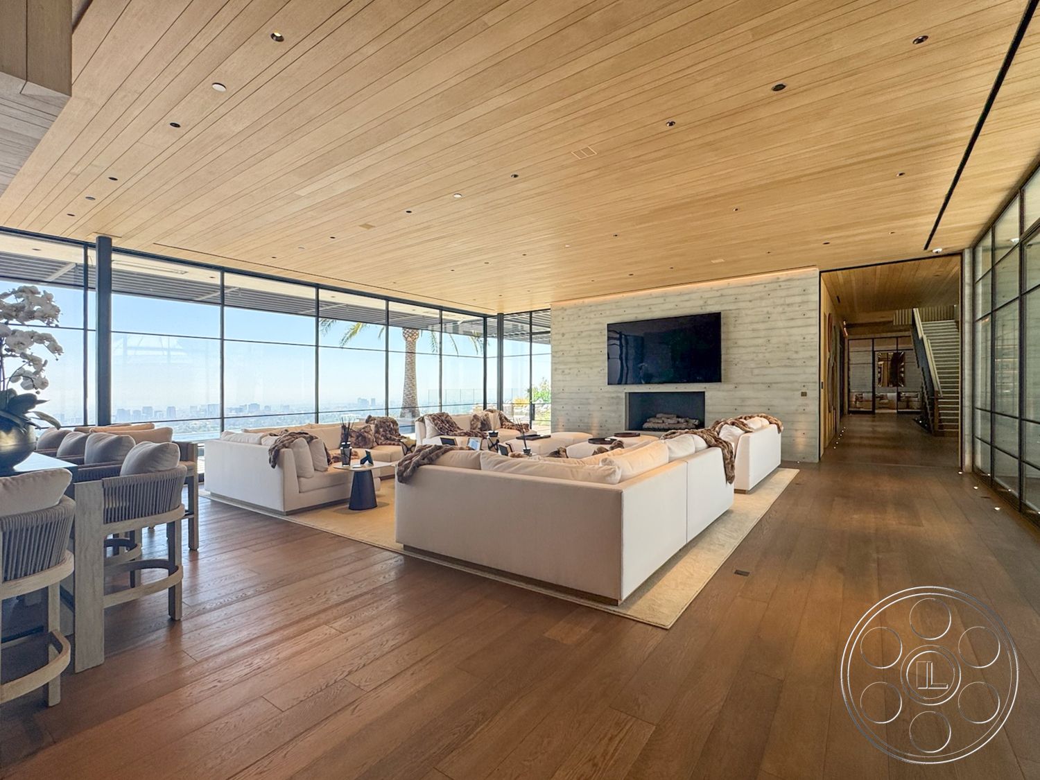 Star Villa - hardwood flooring, glass sliding doors, floor-to-ceiling windows, white sectional sofa, open-concept layout, contemporary living room, plank ceiling, natural light-filled space, wood beam ceiling, stone fireplace wall, hanging pendant lighting, modern entertainment wall, sandy beige area rug, living room with city skyline view