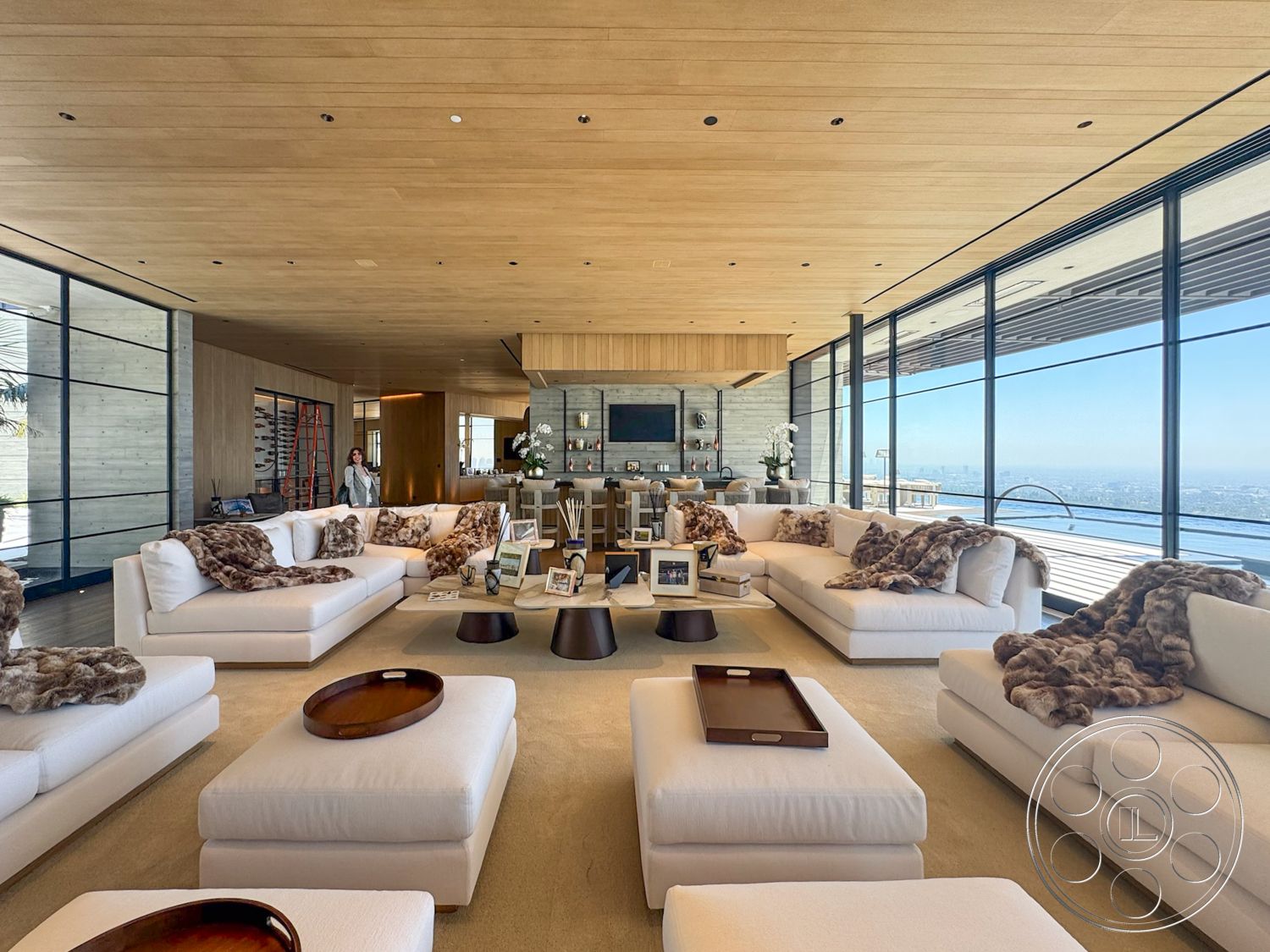 Star Villa - stone fireplace, floor-to-ceiling windows, open-concept living space, city skyline view, modern minimalist style, concrete accent wall, wood paneled ceiling, light beige carpet flooring, cream upholstered sofas, textured fur throw blankets, round wooden coffee tables