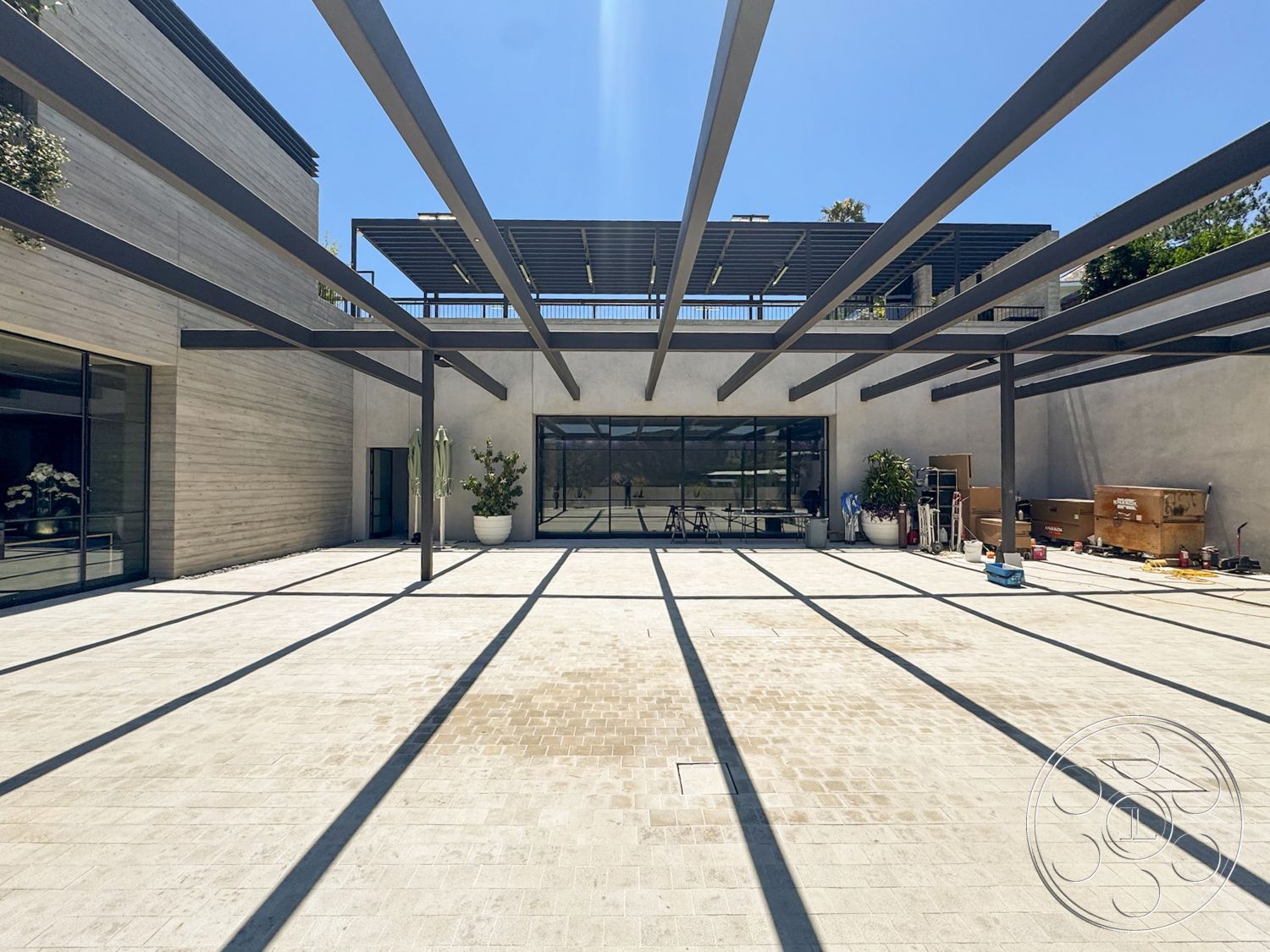 Star Villa - exterior, minimalist aesthetic, outdoor living space, concrete patio flooring, stucco wall finish, natural light exposure, modern architectural design, floor-to-ceiling glass doors, wood panel accent wall, steel pergola structure, open courtyard layout, planters with decorative greenery, linear shading from overhead beams