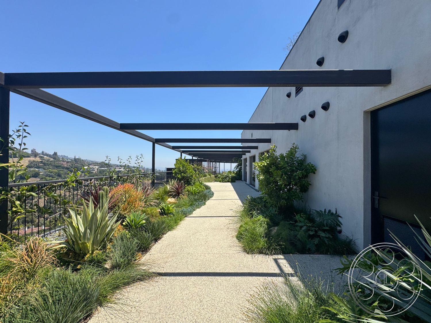 Star Villa - exterior, white stucco walls, modern architectural style, concrete walkway, black metal railings, drought-resistant plants, flat roof design, mountain view setting, landscaped garden borders, metal pergola structure, open air pathway