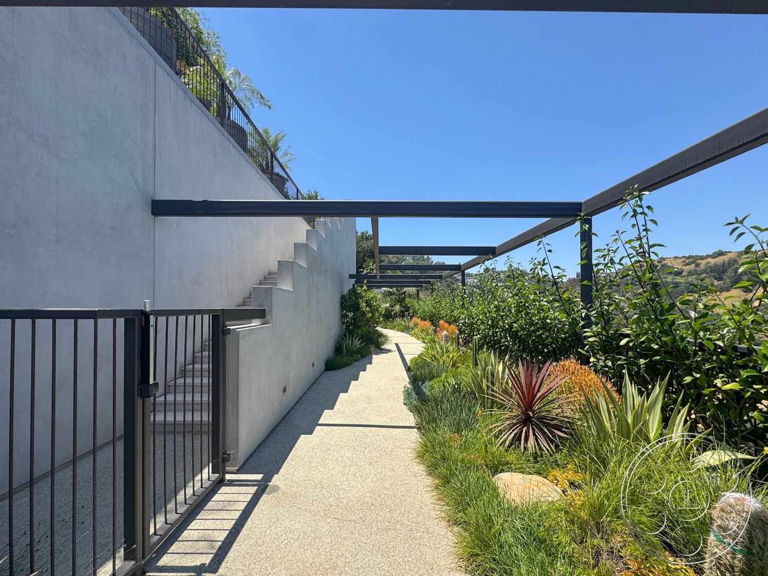 Star Villa - exterior, concrete wall, textured plaster walls, outdoor pathway, hillside location, garden flora, metal pergola structure, landscape planting beds, metal railing gate, cement pathway, stairs with concrete steps