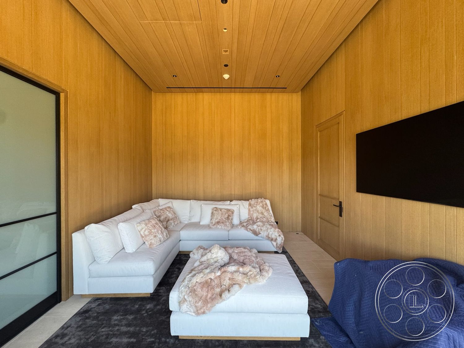Star Villa - neutral color palette, glass door, dark area rug, textured throw blankets, recessed ceiling lighting, upholstered sectional sofa, wood paneling walls, minimalist wall-mounted television, smooth hardwood ceiling, white fabric cushions