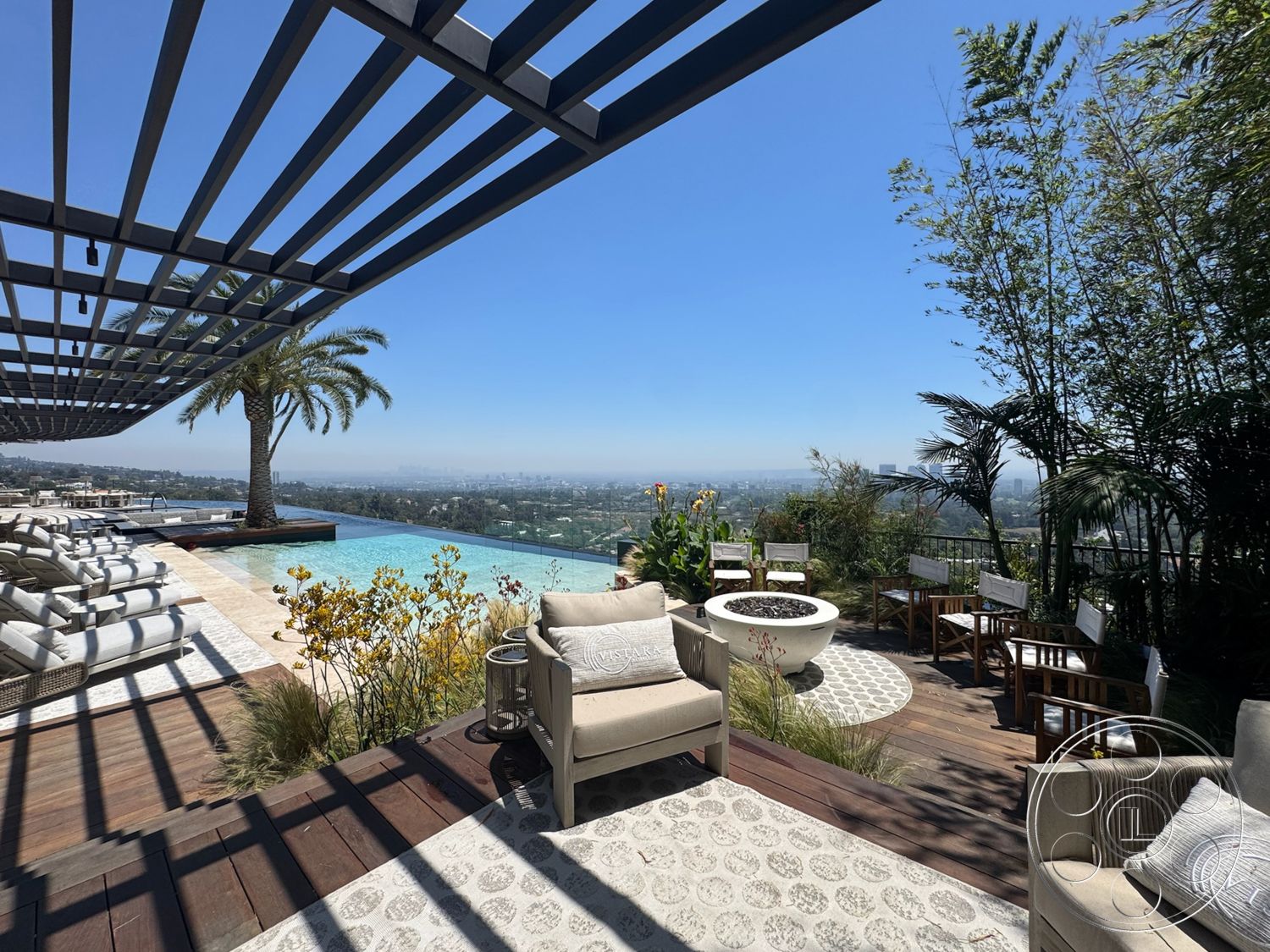 Star Villa - exterior, palm trees, woven outdoor furniture, infinity pool, concrete pool deck, wooden deck flooring, panoramic city skyline view, landscaped garden with tropical plants, metal pergola structure, textured stone patio flooring, fire pit with circular stone surround, ceramic tile detail, sun loungers arranged around pool