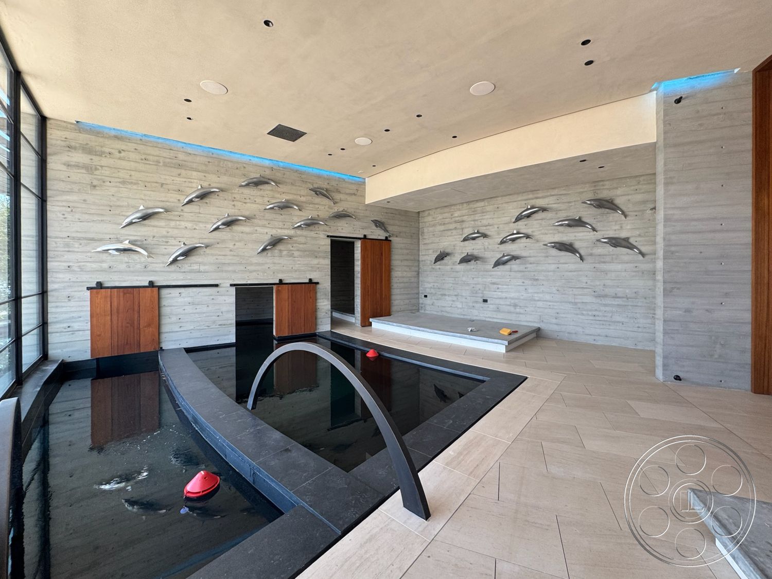 Star Villa - concrete walls, floor-to-ceiling windows, modern architectural style, exposed ceiling, rectangular pool, light-colored tile flooring, wood accent cabinetry, black stone pool border, faux dolphin wall art, water feature area