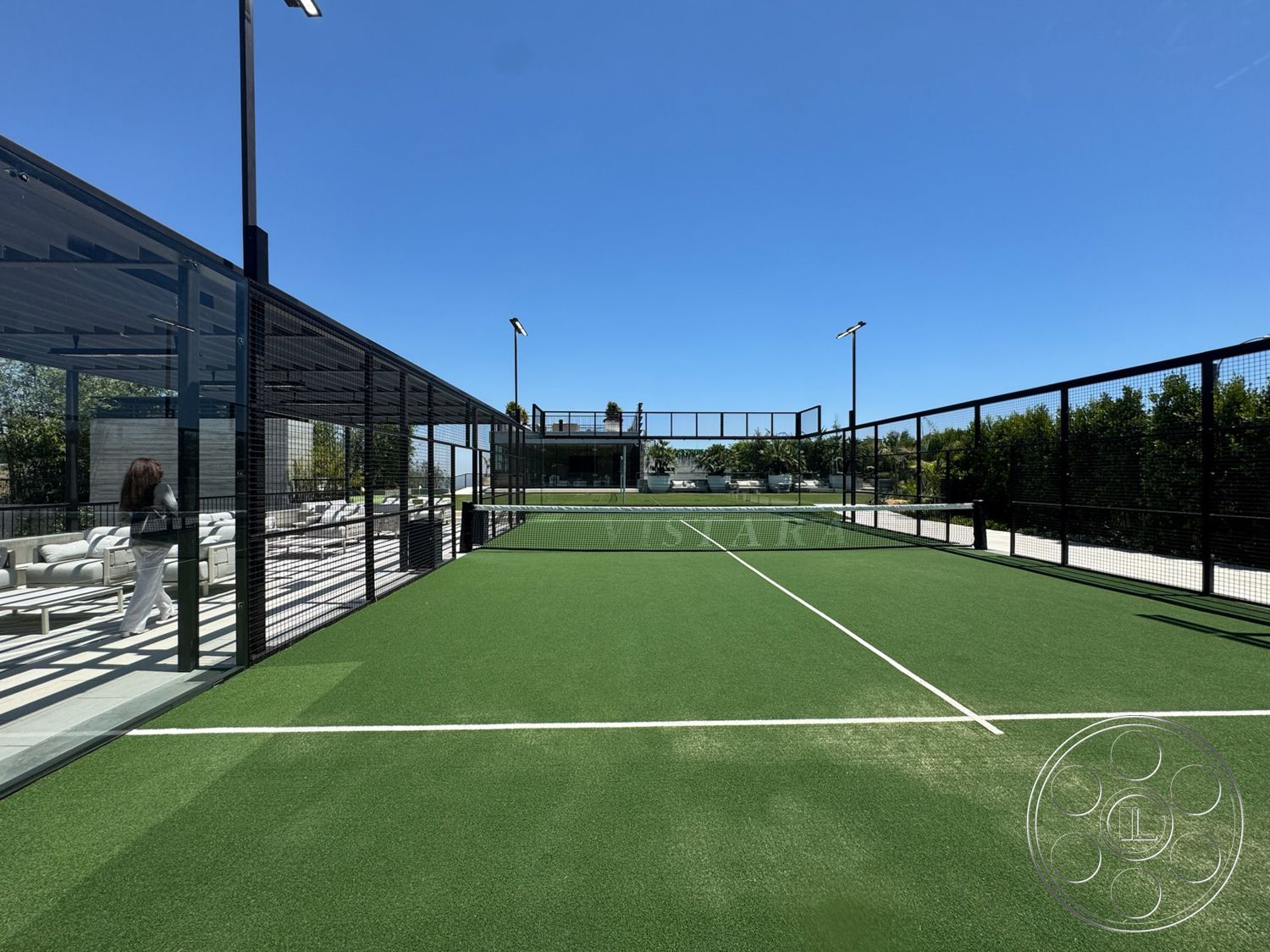 Star Villa - exterior, lush greenery backdrop, modern outdoor lounge area, metal light fixtures, sunny outdoor setting, concrete patio flooring, glass wall structure, artificial turf tennis court, perimeter fence with netting