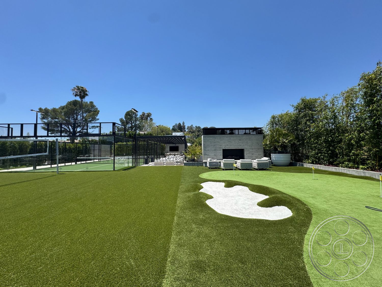 Star Villa - exterior, open outdoor space, artificial turf lawn, concrete seating area, modern architectural design, sunny backyard setting, stone fireplace feature, black metal fencing, landscape planting beds, modular outdoor furniture, custom putting green with sand trap