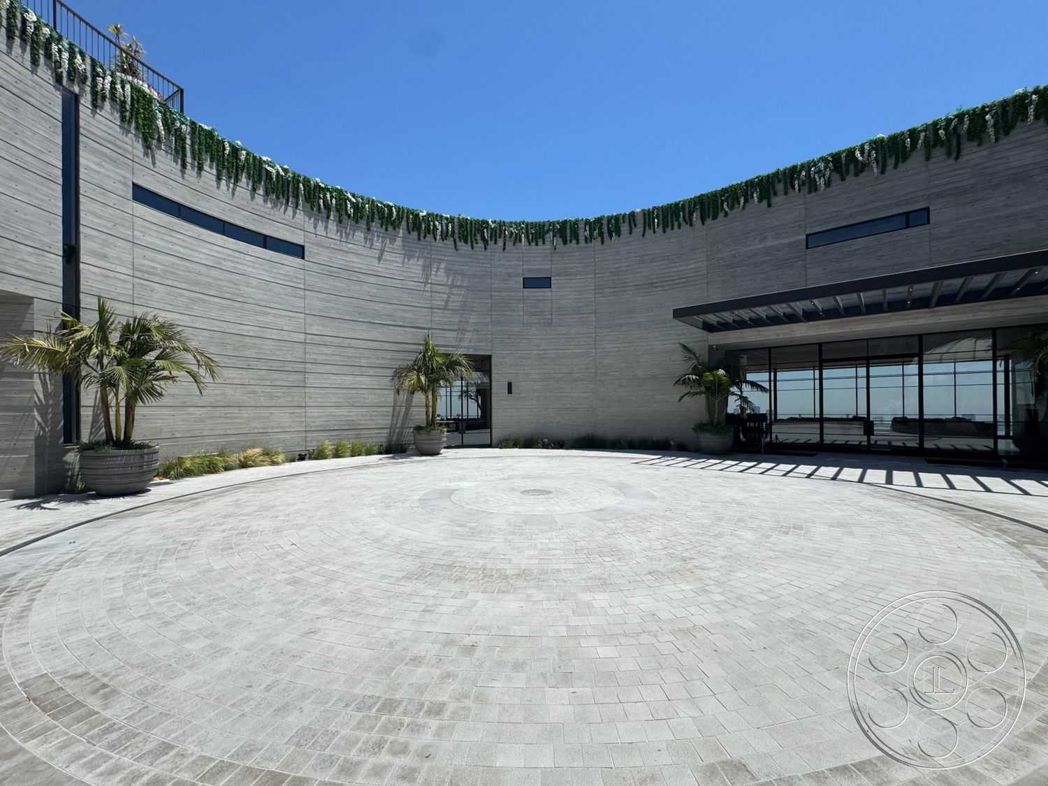 Star Villa - exterior, floor-to-ceiling windows, landscaped courtyard, textured concrete surface, modern architectural design, curved concrete walls, greenery on roof edge, circular paver driveway, palm trees in planter pots, horizontal slatted roof overhang