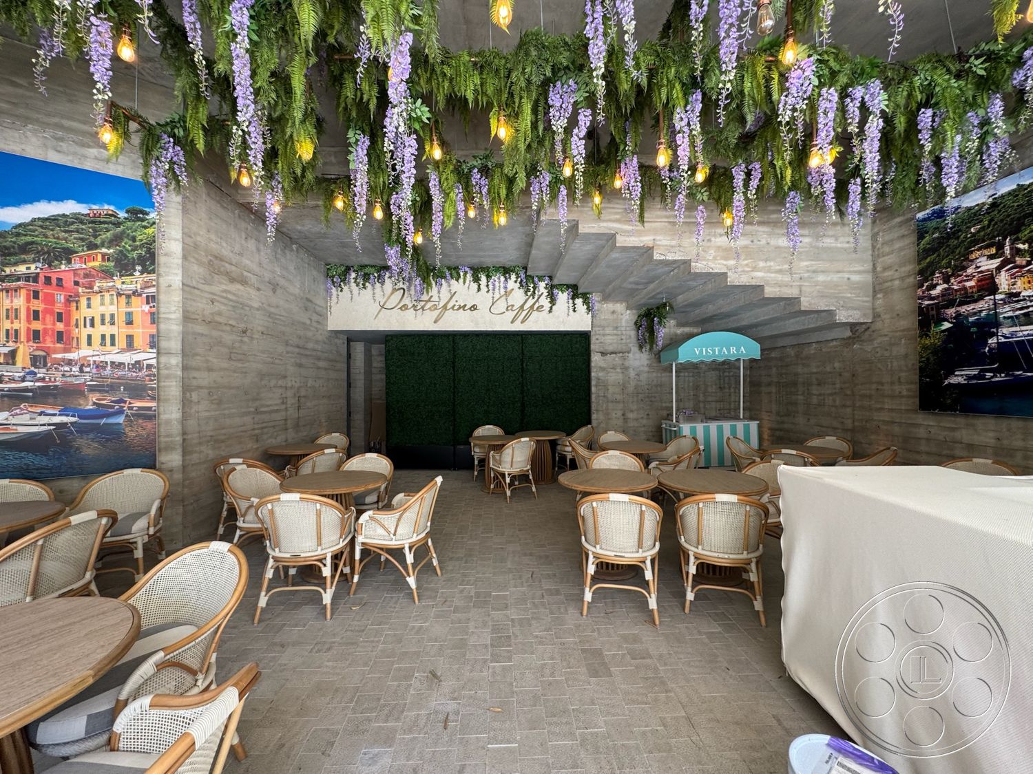 Star Villa - exposed concrete walls, hanging pendant lights, concrete ceiling, hexagonal tile flooring, greenery accent wall, woven rattan chairs, interior restaurant space, wooden bistro tables, floral overhead decoration, artwork featuring coastal scenery