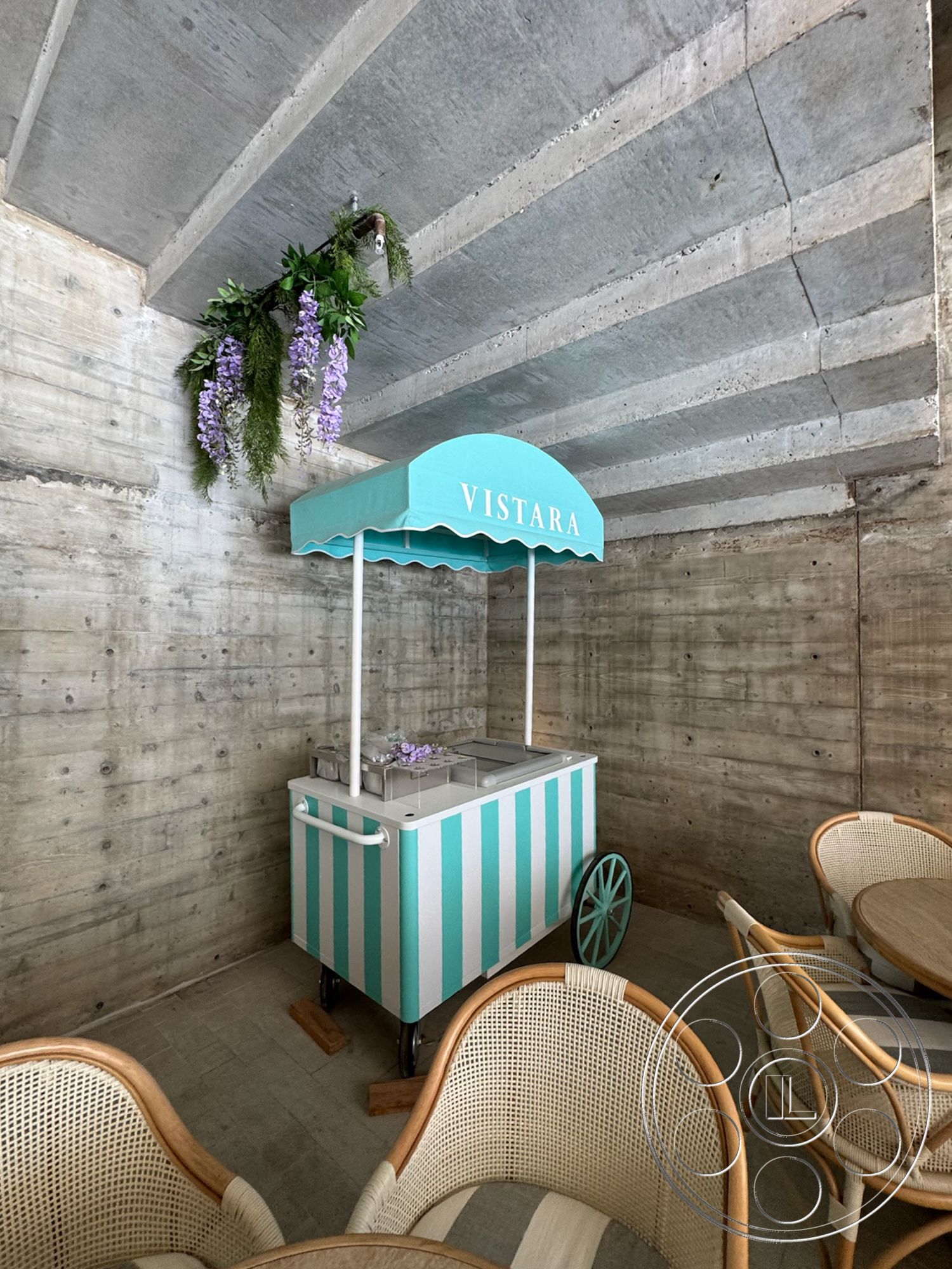 Star Villa - interior space, exposed concrete walls, exposed concrete ceiling, gray concrete flooring, round wooden dining tables, woven rattan chairs, metal ice cream cart, turquoise awning with white lettering
