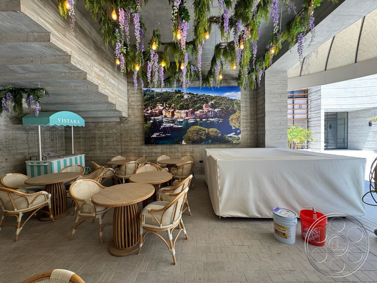 Star Villa - exposed concrete walls, floor-to-ceiling glass windows, stone patio flooring, textured concrete ceiling, wooden round dining tables, woven rattan chair frames, vertical planters with hanging plants, colorful wall mural, light fixtures with bulbs, beach-themed snack stand, modern casual dining area