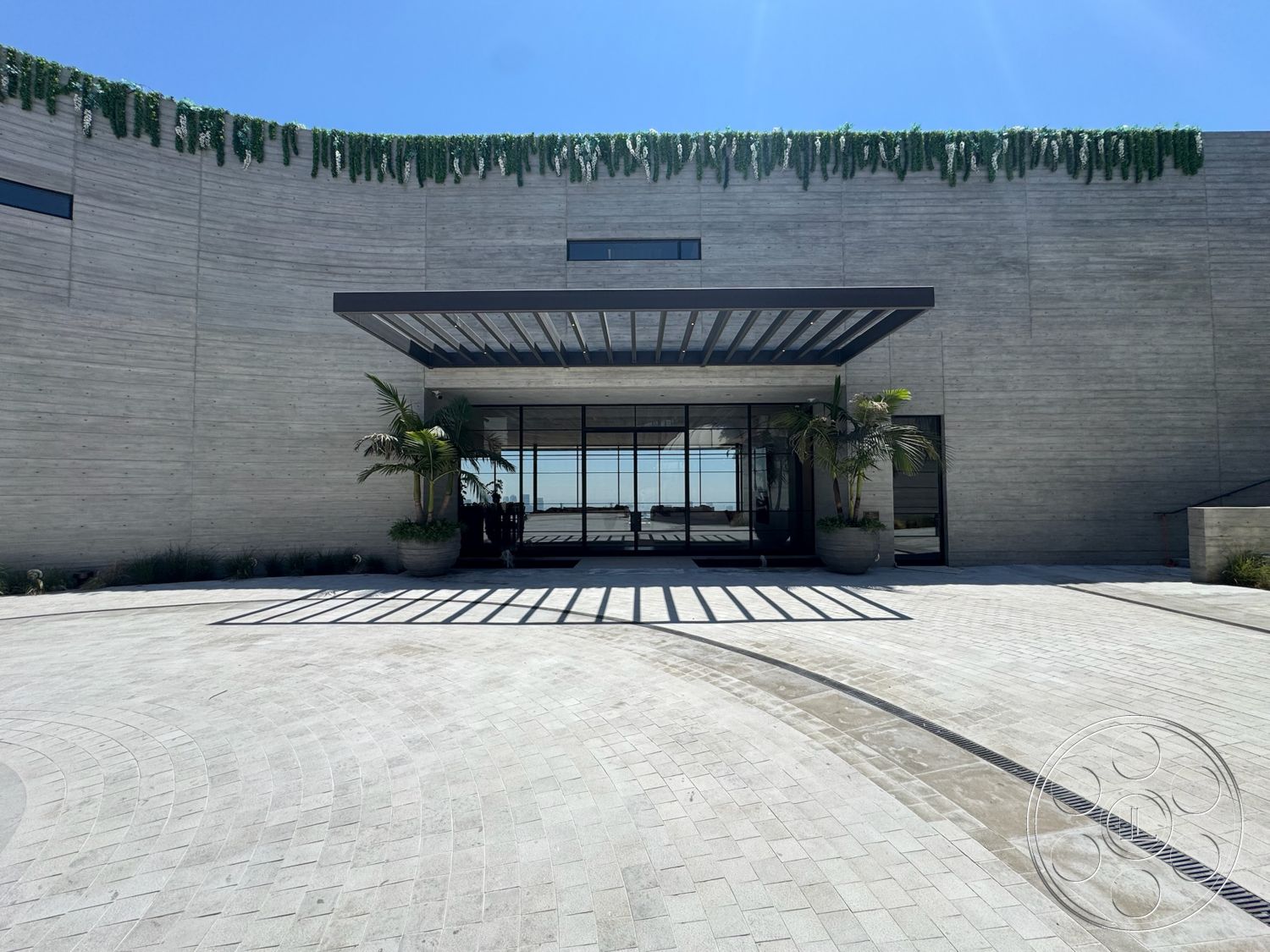 Star Villa - exterior, flat roof, paver driveway, large glass windows, concrete walls, modern architectural style, landscaped entryway, glass entrance doors, curved driveway design, horizontal wood slat canopy, outdoor greenery accents