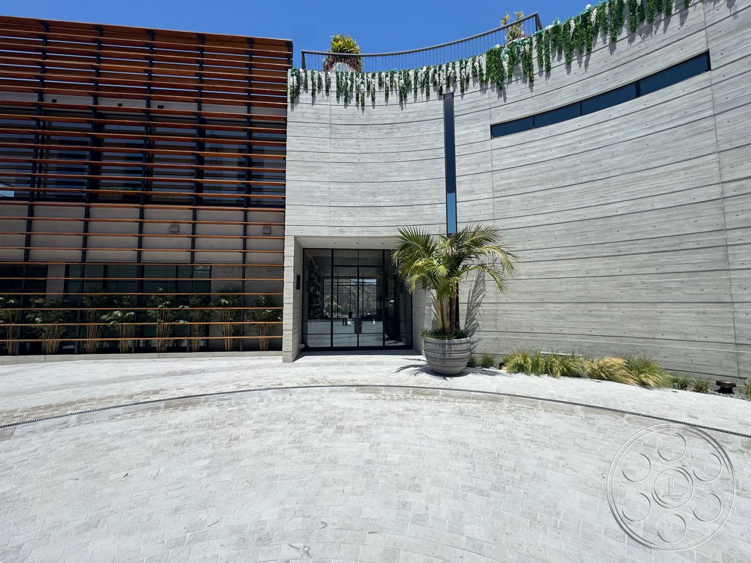 Star Villa - large windows, exterior, concrete walls, modern architectural style, curved architecture, horizontal wooden slats, glass entry doors, stone paver driveway, wood slat facade, landscaped planter with palm tree