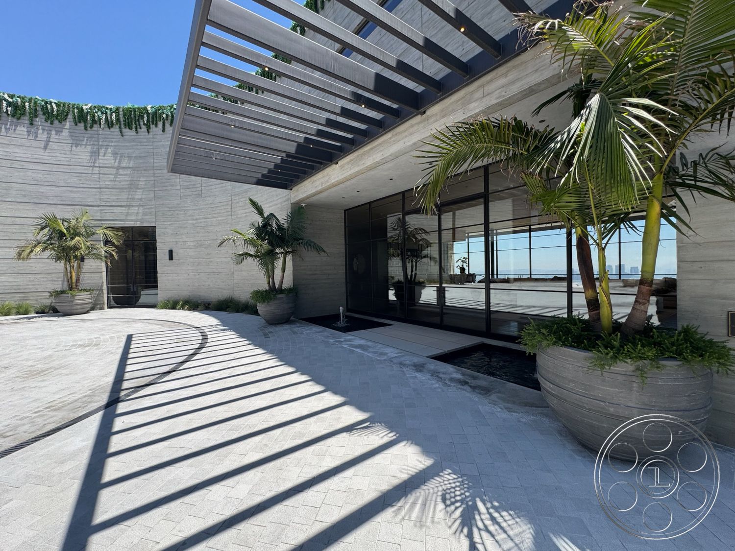Star Villa - exterior, landscaped garden, natural stone accents, concrete walls, modern architectural style, concrete driveway, concrete path, outdoor lighting fixtures, textured concrete surface, horizontal wooden slats, glass entry doors, shaded outdoor area, rectangular entryway, curved building shape, potted palm trees, steel roof overhang