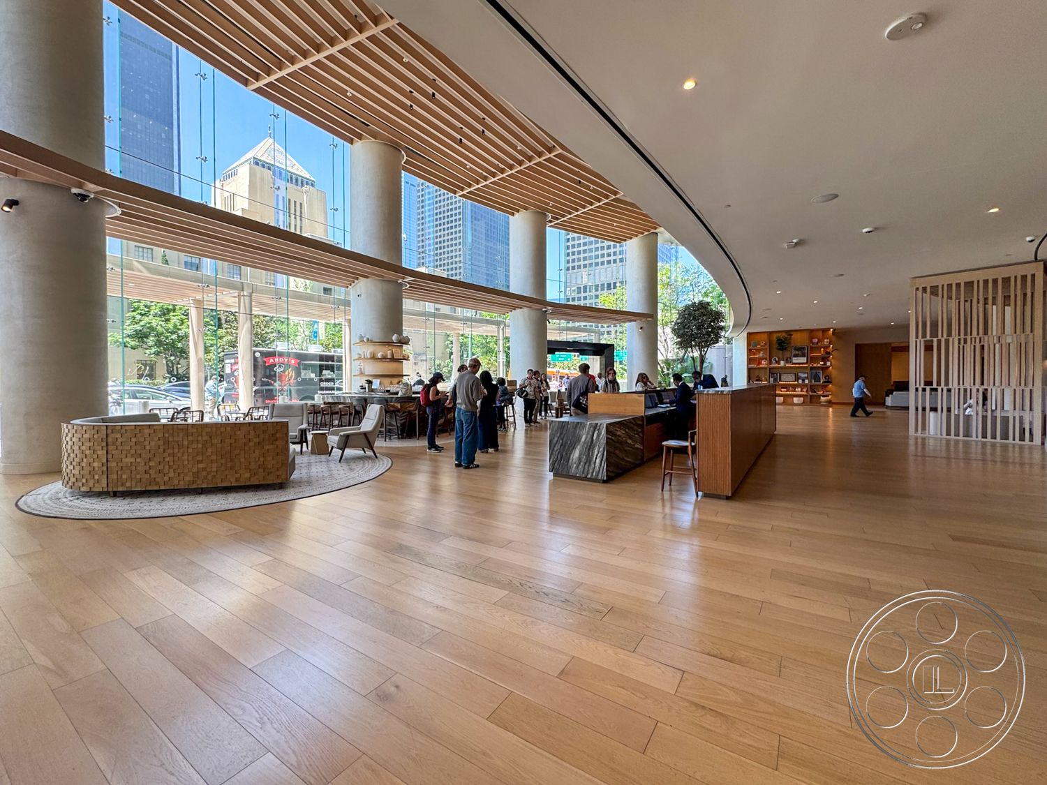 Office 123 - natural light, hardwood flooring, open floor plan, modern furniture, large glass windows, urban setting, reception area, textured wall treatment, circular area rug, exposed concrete columns, curved ceiling design, wood slat ceiling details, wooden decorative shelving