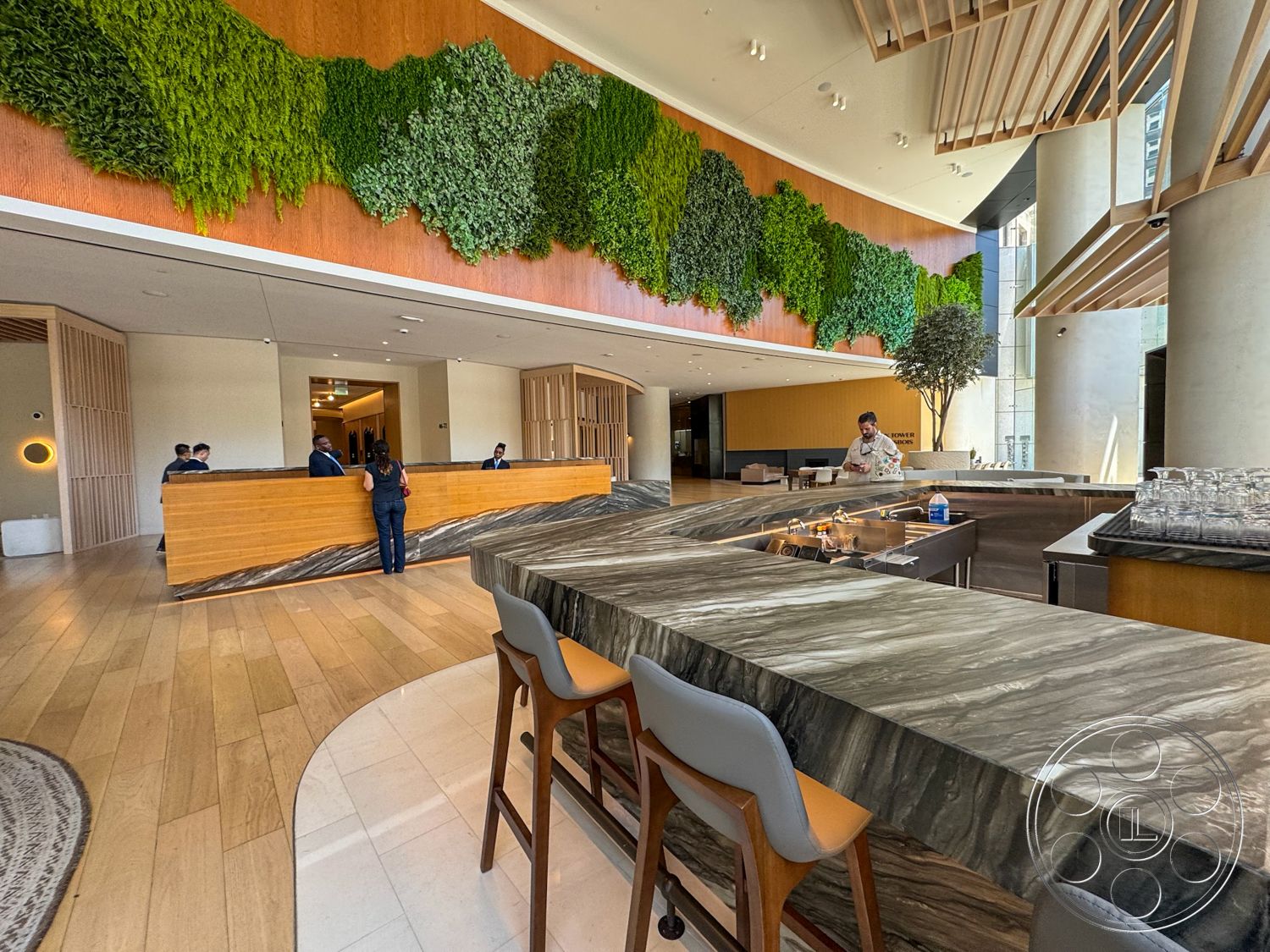 Office 123 - indoor plants, open layout, light wood flooring, modern lighting fixtures, textured plaster walls, wooden reception desk, exposed concrete columns, curved bar design, luxury marble bar countertop, greenery wall art, accent decorative wall