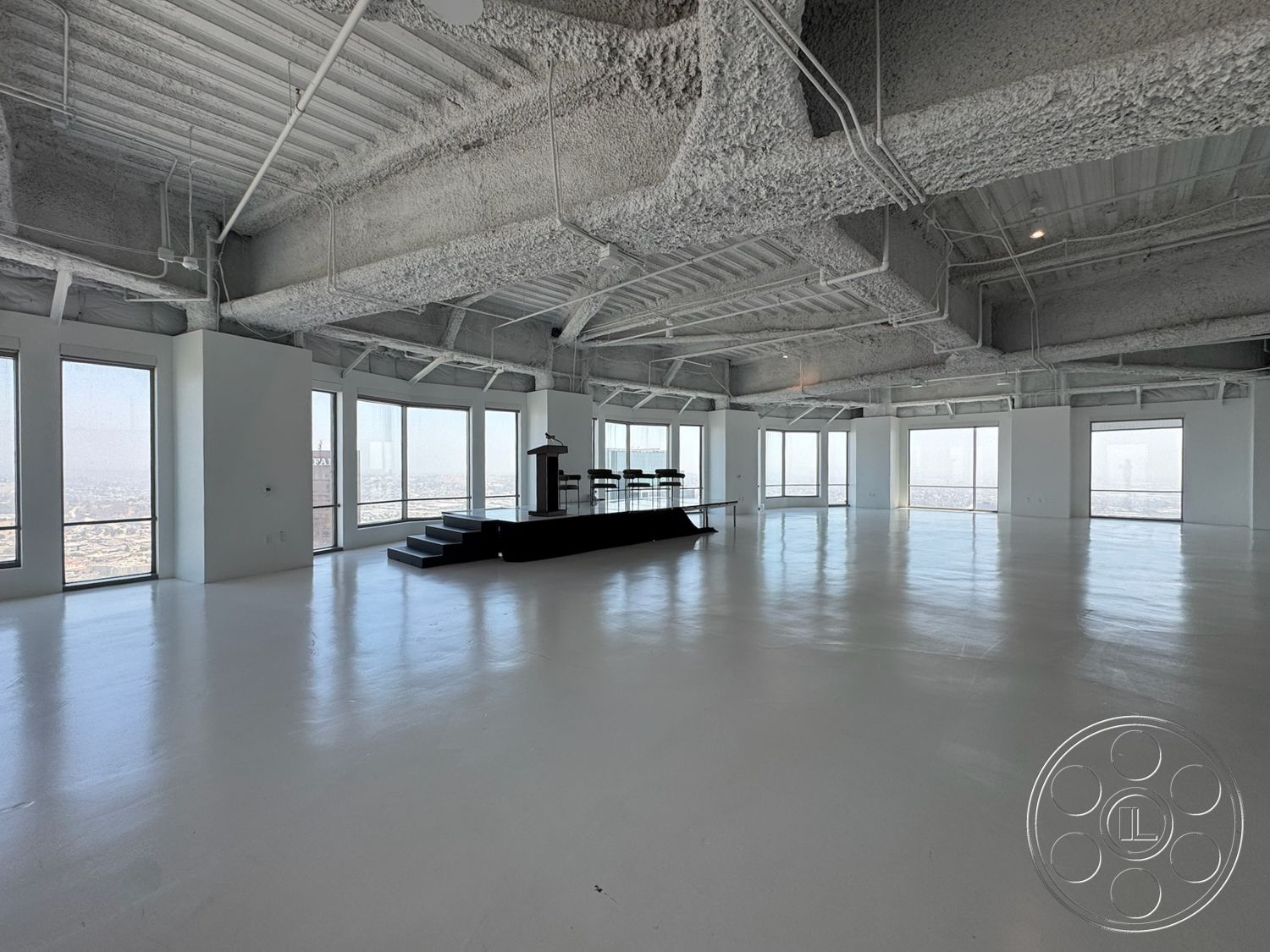 Office 123 - open floor plan, concrete floor, interior space, floor-to-ceiling windows, modern architectural style, city skyline view, exposed concrete ceiling, white painted walls, industrial-style lighting fixtures, black podium stage