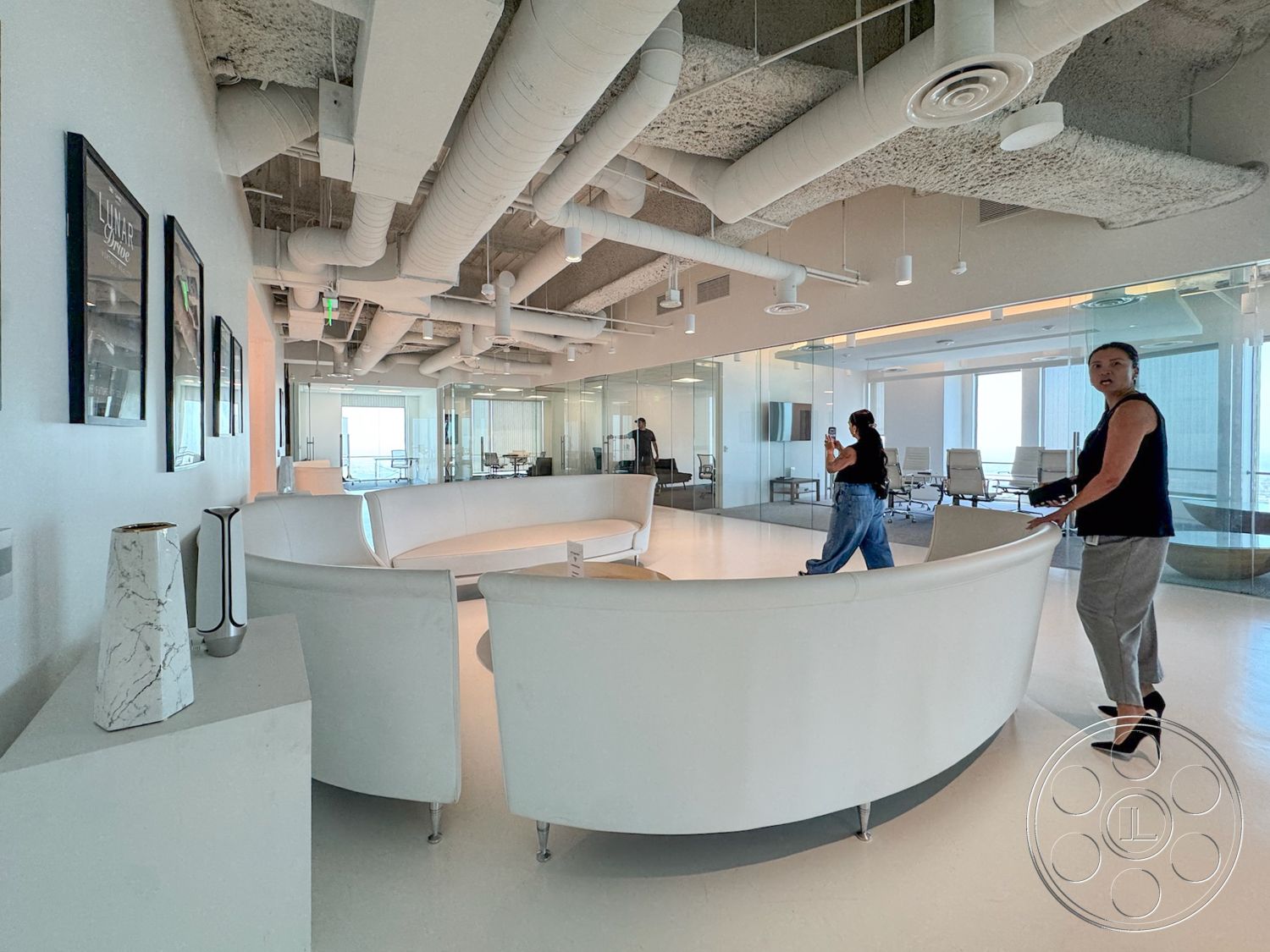 Office 123 - minimalist design, open floor plan, bright natural light, polished concrete flooring, glass partition walls, modern office setting, exposed ductwork ceiling, white curved seating area, decorative wall art frames