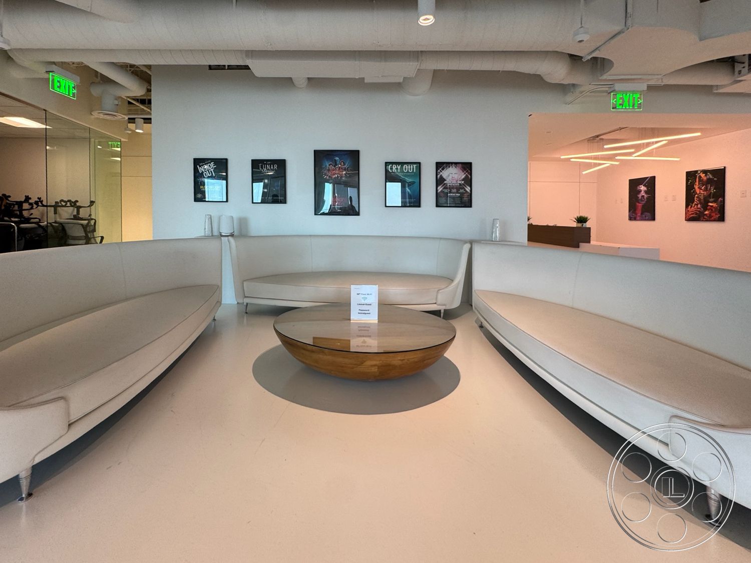 Office 123 - open space layout, ambient lighting fixtures, interior lounge area, exposed ductwork ceiling, curved white upholstery sofas, circular wood coffee table, light-colored polished concrete floor, framed artwork wall displays, minimalist aesthetic design
