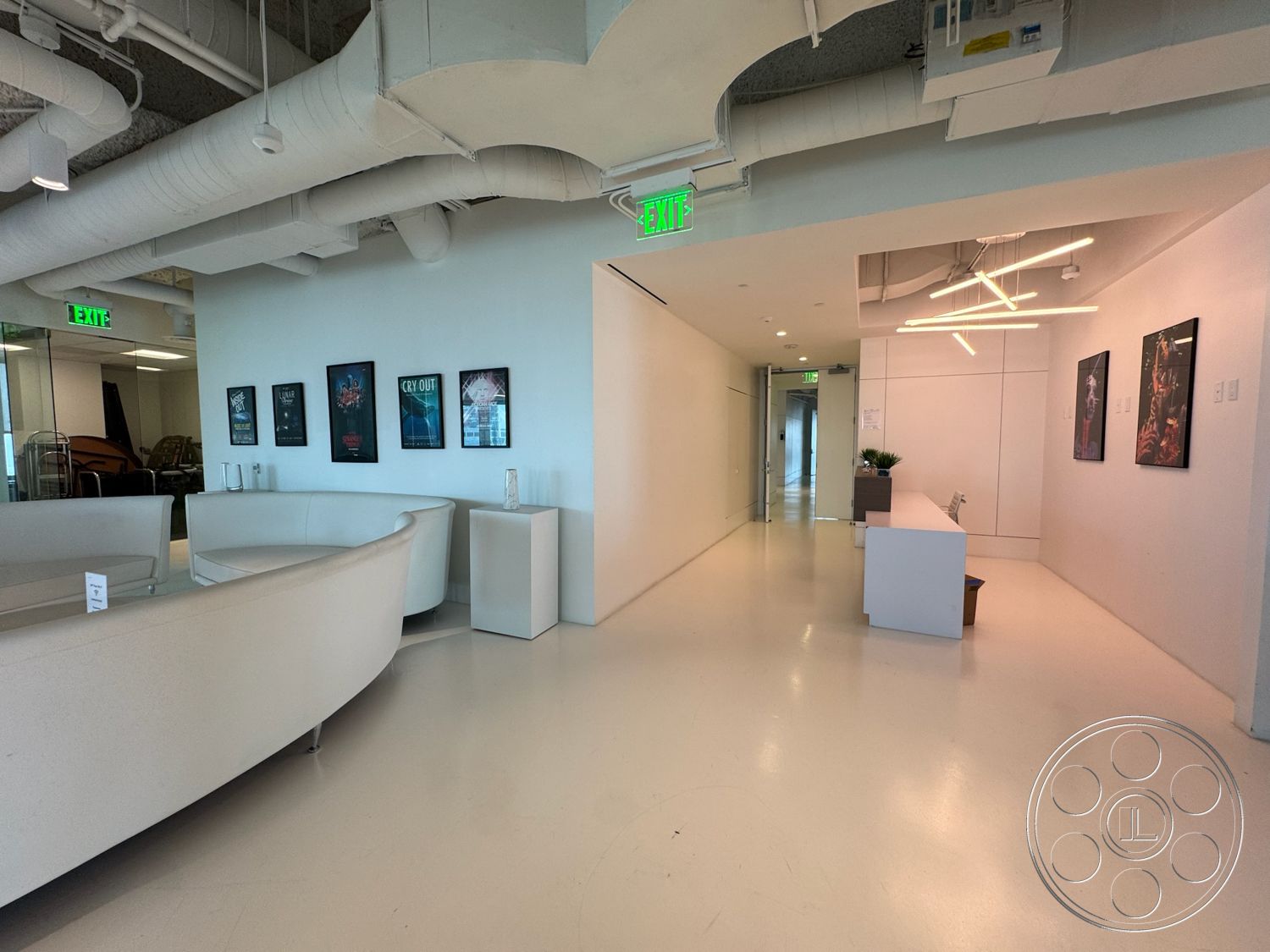 Office 123 - white walls, glass door, clean lines, minimalist design, polished concrete flooring, modern light fixtures, interior space, exposed ceiling ducts, curved white sofa, art wall with framed posters