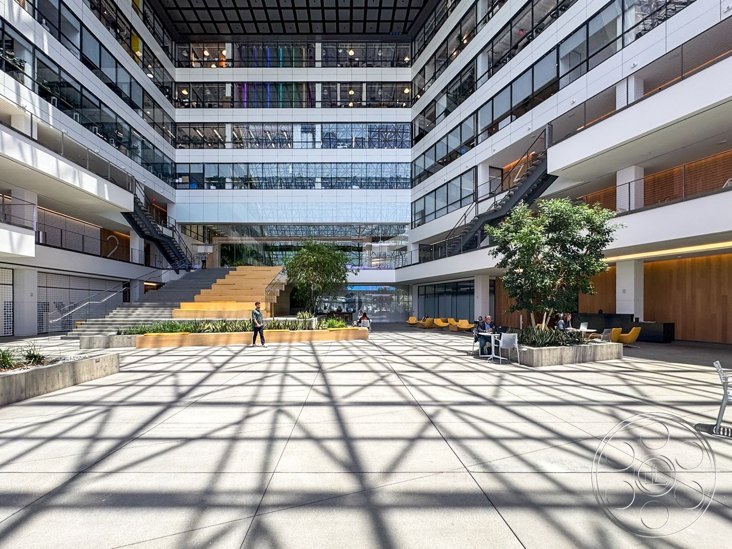 The Atrium - natural light, exterior, urban setting, modern architectural style, textured concrete planters, steel staircase, floor-to-ceiling glass windows, open atrium design, green landscaping elements, concrete plaza flooring, vegetation accents, horizontal metal railing, glass curtain walls, wooden seating steps, multipurpose public space
