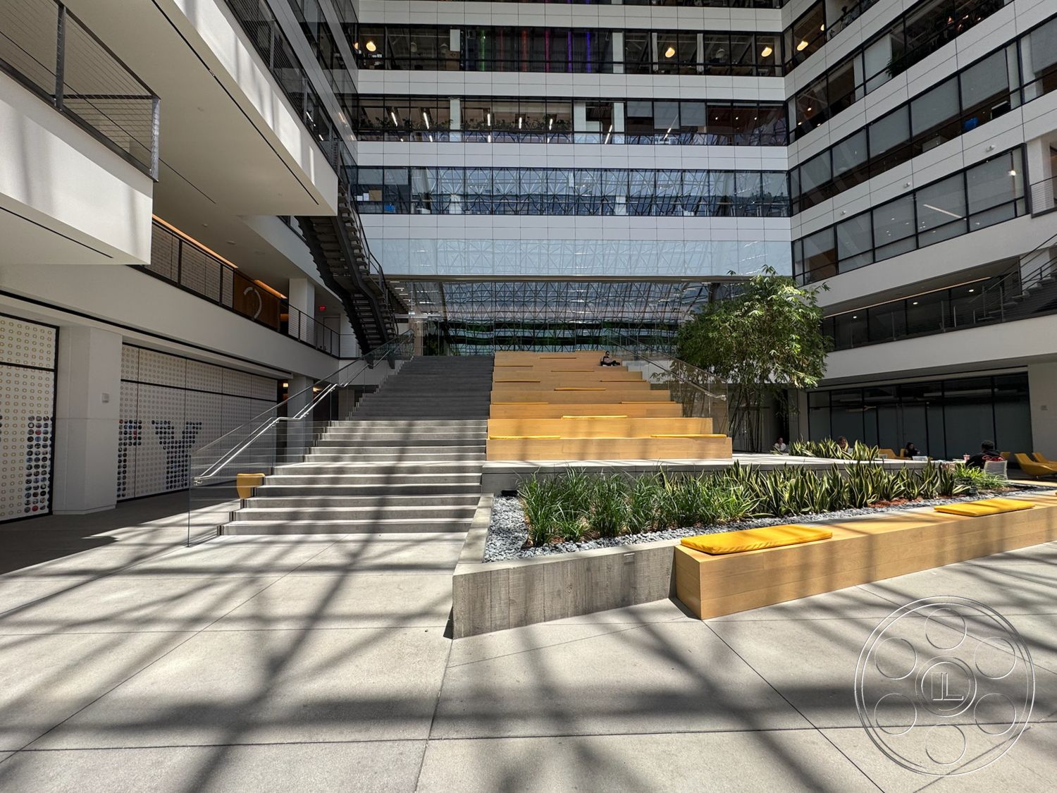 The Atrium - exterior, landscaped greenery, urban setting, floor-to-ceiling windows, concrete steps, open-air courtyard, steel railing, concrete walkway, modern architectural design, wood seating, bamboo planter boxes, glass atrium, yellow cushions, suspension stairway