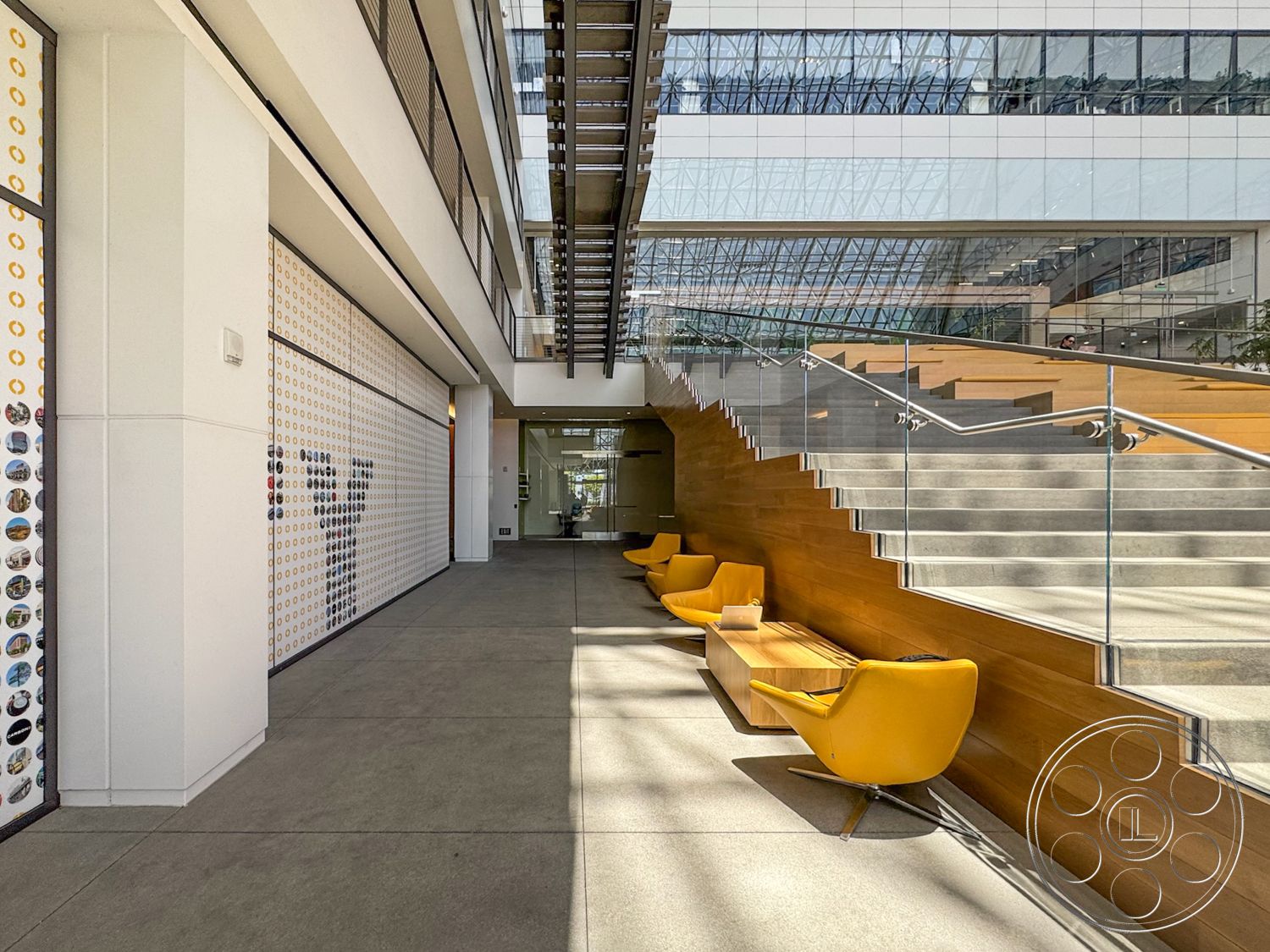 The Atrium - large windows, natural lighting, concrete floor, glass walls, high ceiling, textured wall treatment, modern lounge chairs, minimalist architectural style, open atrium design, wood bench seating, exposed steel staircase, wooden staircase risers, yellow seating