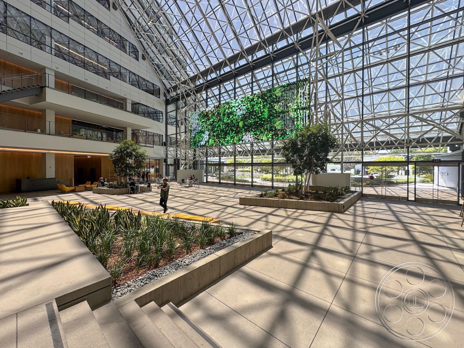 The Atrium - concrete flooring, urban setting, planter boxes, modern architectural style, natural light exposure, exposed steel framework, stainless steel stair railings, open seating area, glass atrium roof, wood paneling wall accents, indoor greenery landscaping, integrated digital display wall, skylight lighting, two-story atrium space