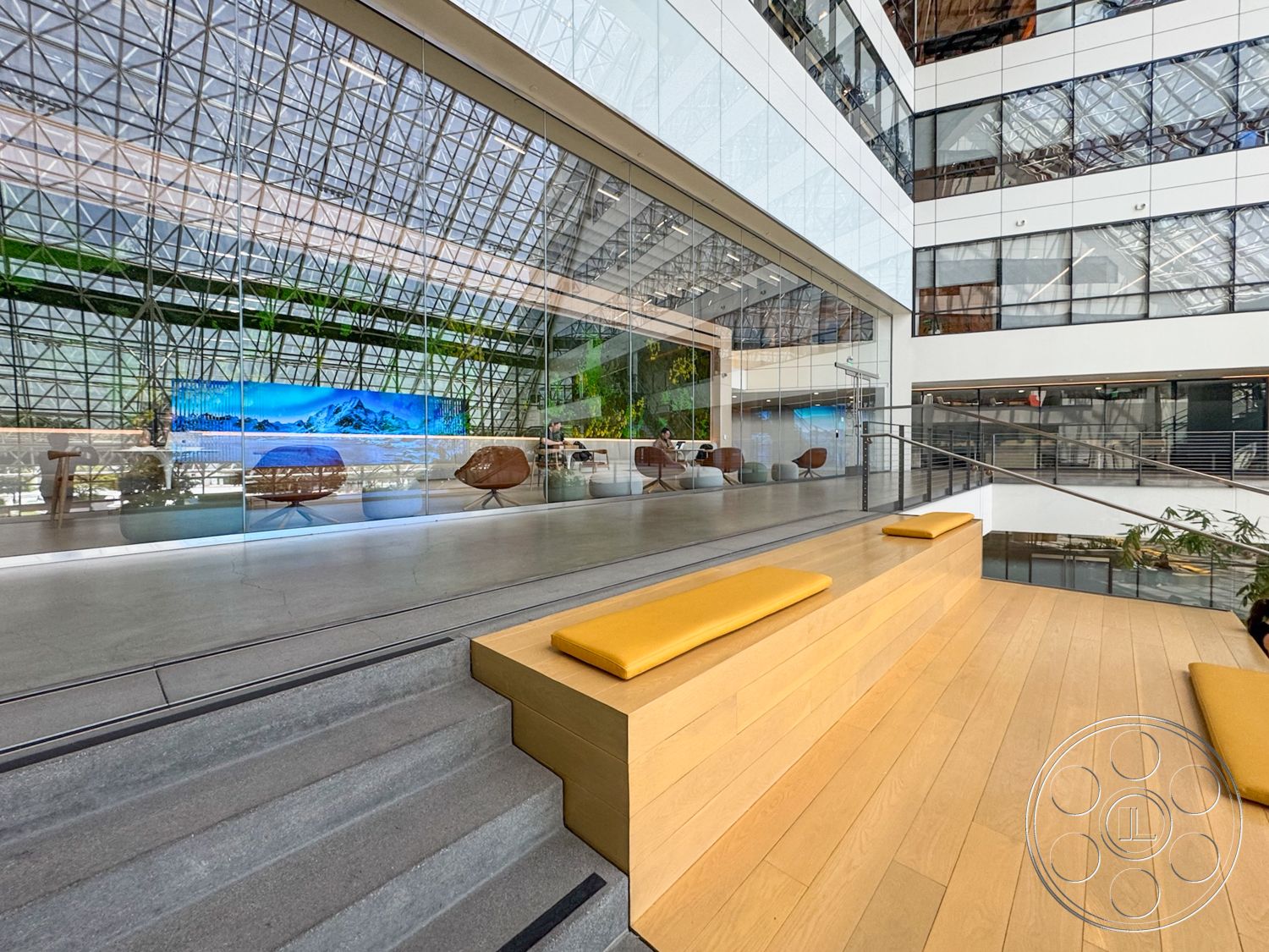 The Atrium - natural light, exterior, minimalist design, floor-to-ceiling windows, industrial lighting fixtures, modern architectural style, furniture arrangement, glass curtain wall, exposed steel frame, large skylight, open atrium, wooden seating steps, concrete base floor, indoor plant greenery, view of surrounding landscape
