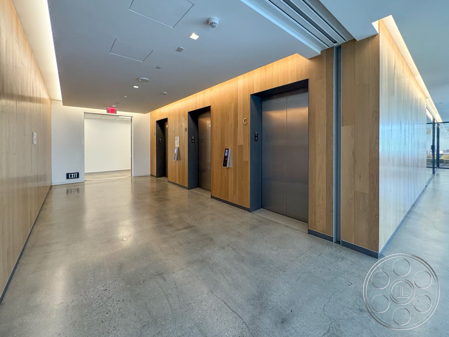 The Atrium - high ceilings, minimalist design, concrete flooring, modern lighting fixtures, glass partitions, exit sign, commercial space, elevator doors, steel structural elements, wood panel wall treatment, straight hallway