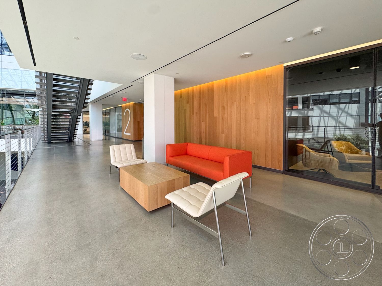 The Atrium - open floor plan, floor-to-ceiling windows, wood accent wall, metal railing staircase, rectangular coffee table, glass partition walls, minimalist architectural style, modern lounge seating, interior lobby space, exposed concrete flooring
