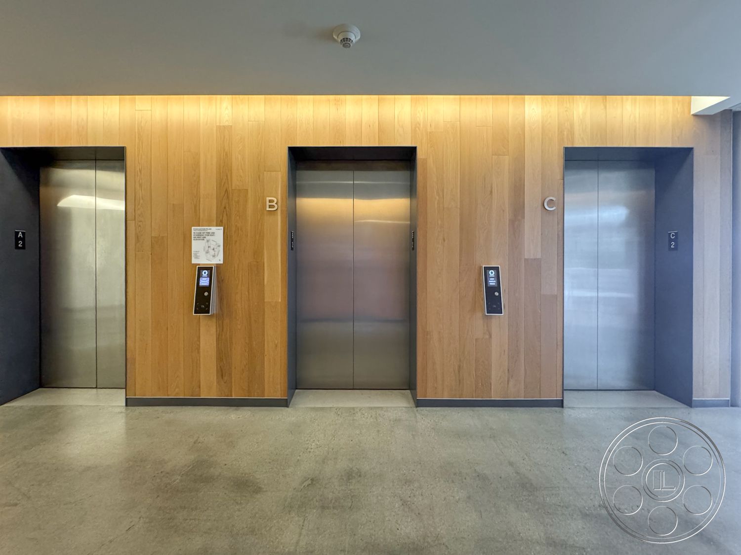 The Atrium - concrete floor, illuminated ceiling, commercial space, modern architectural design, minimalist interior, wood panel wall treatment, exterior elevator bank, steel elevator doors, three elevator shafts