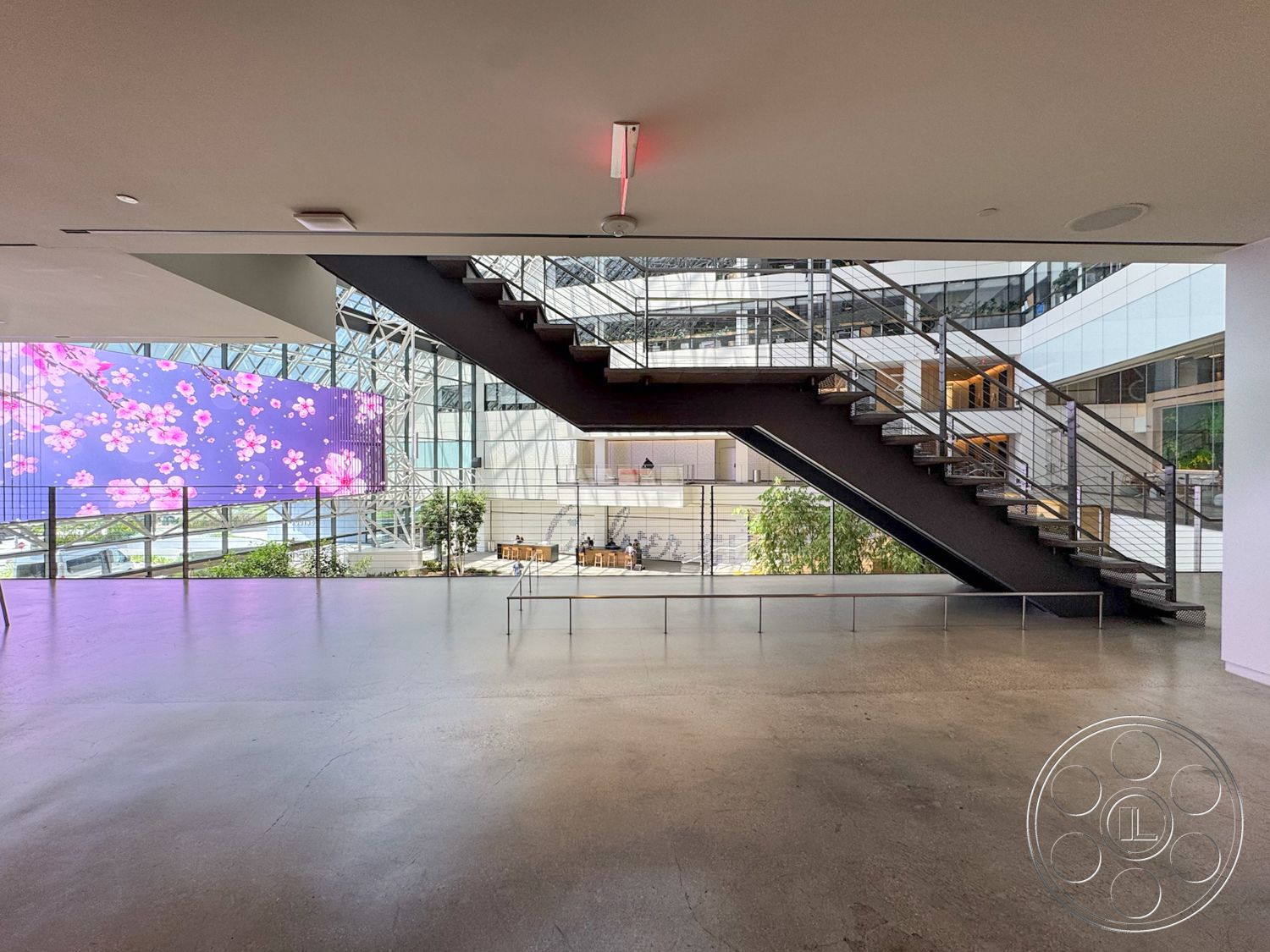 The Atrium - natural light, concrete floor, glass railing, modern architectural style, metal staircase, open atrium space, exposed structural framework, landscaped indoor area, LED display wall