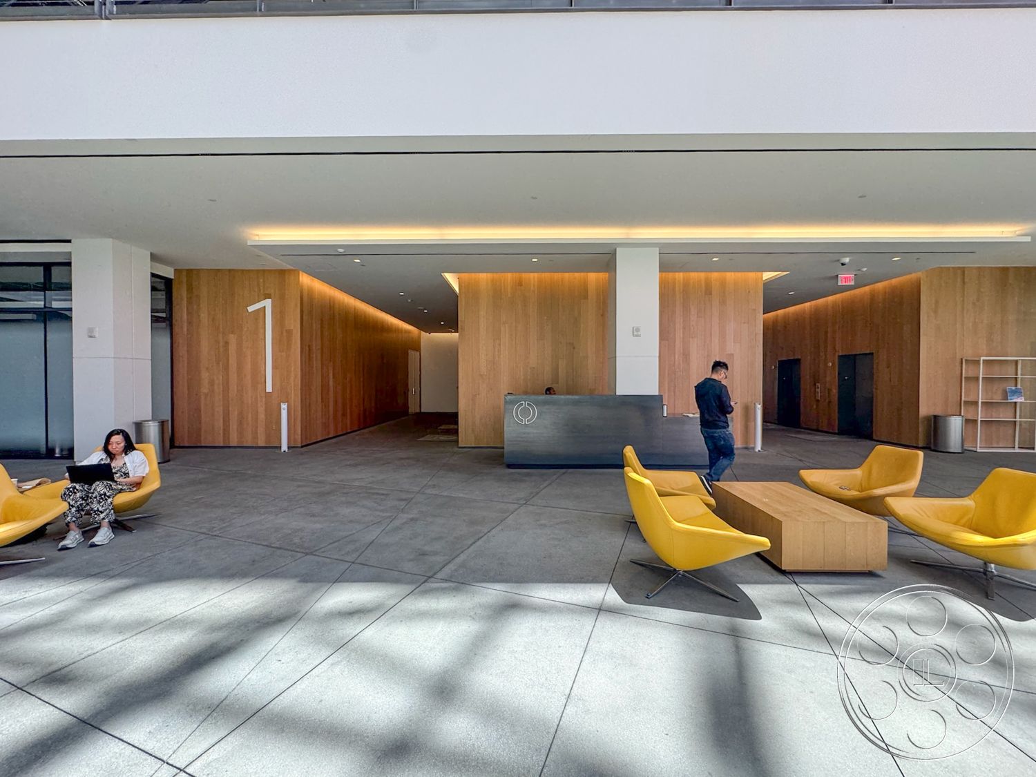 The Atrium - exterior, natural lighting, concrete flooring, urban setting, textured ceiling, square coffee table, glass partition walls, minimalist interior design, open lobby space, wood panel accent wall, modern reception desk, dimensional signage, yellow molded plastic chairs