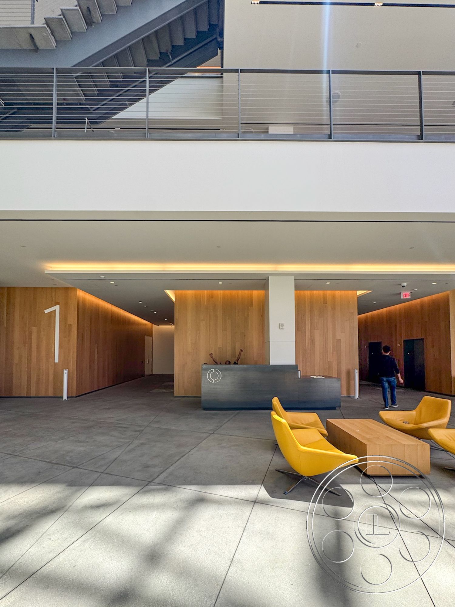 The Atrium - minimalist design, concrete flooring, geometric design elements, floor-to-ceiling windows, textured wall treatments, yellow accent chairs, reception desk, modern lounge seating, wood panel accent wall, LED ceiling lighting, steel stair railing, open lobby area