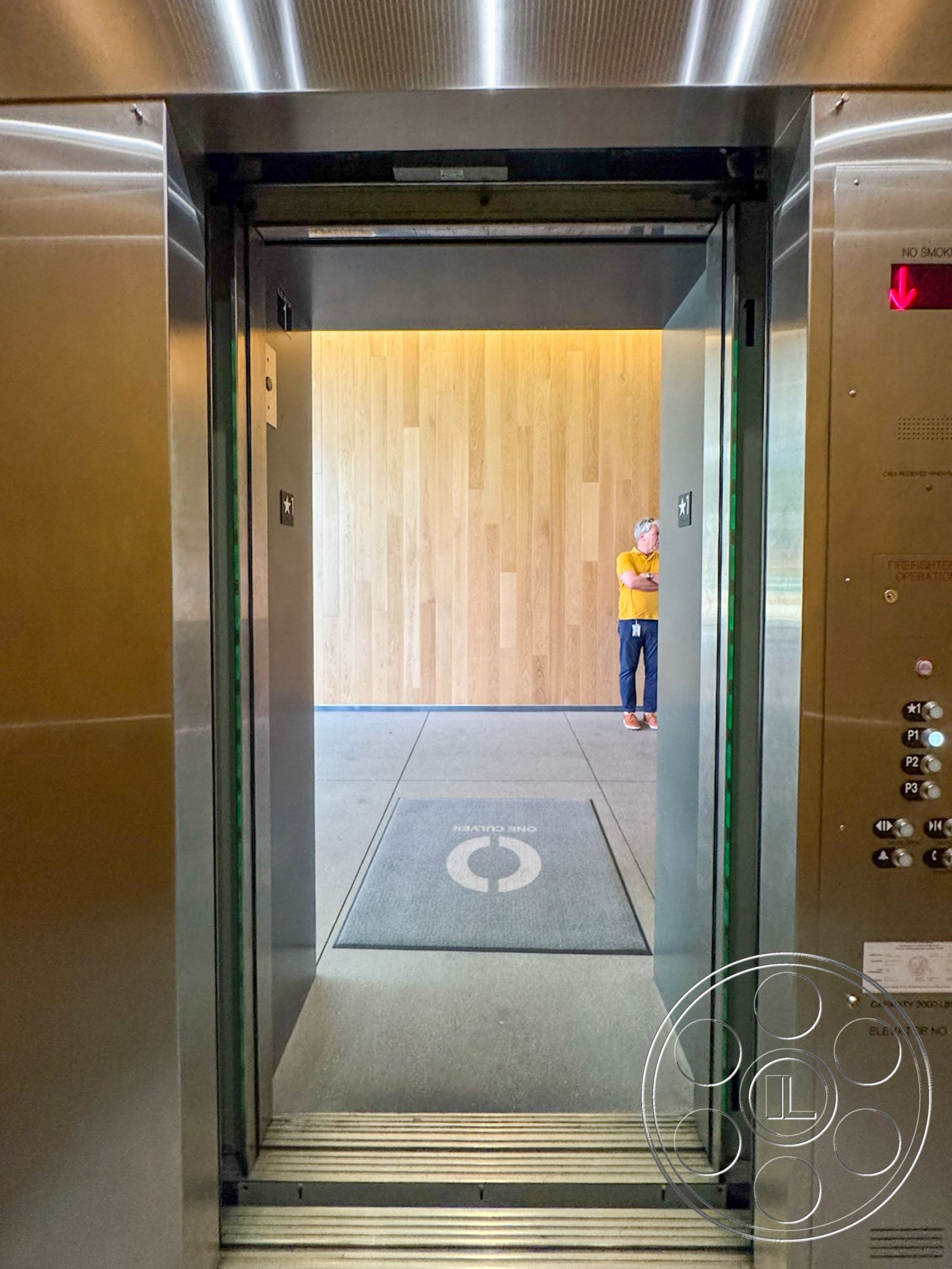 The Atrium - minimalist design elements, smooth concrete flooring, wood accent wall, ground-level entrance, interior elevator lobby, stainless steel elevator doors, commercial elevator interior