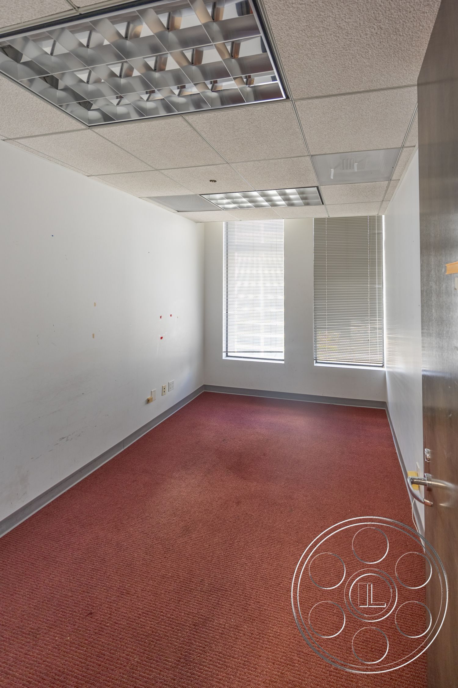 Rooftop 53 - window blinds, white painted walls, drop ceiling tiles, carpet office flooring, fluorescent ceiling lights, gray door frame, two vertical windows